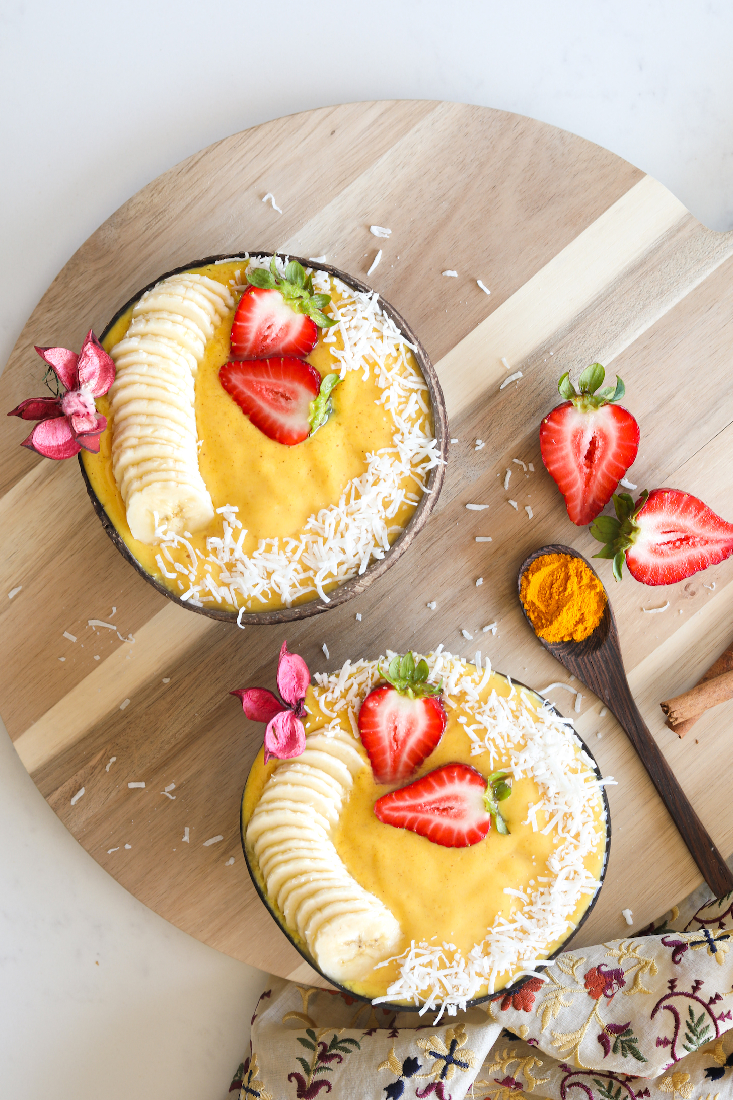 Two bowls of yellow smoothie topped with banana slices and strawberries.