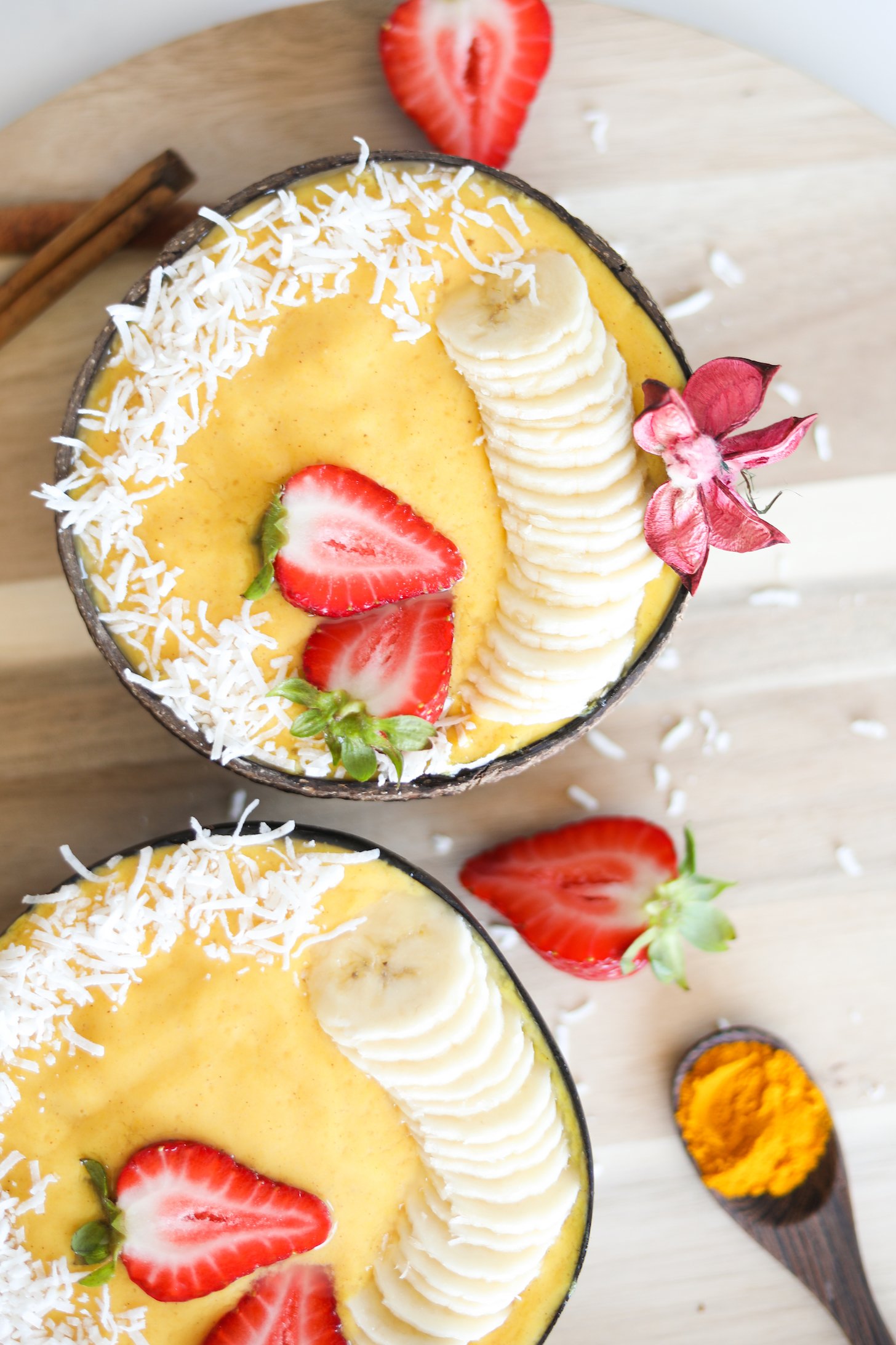 Flatlay image of two bowls of yellow smoothie topped with banana and strawberries.