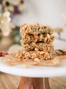 A close up image of a stack of oat bars with peanuts on a white stand.