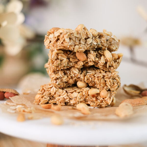 A close up image of a stack of oat bars with peanuts on a white stand.