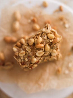 Top view of an oat bar topped with peanuts on a stack of bars surrounded by peanuts.