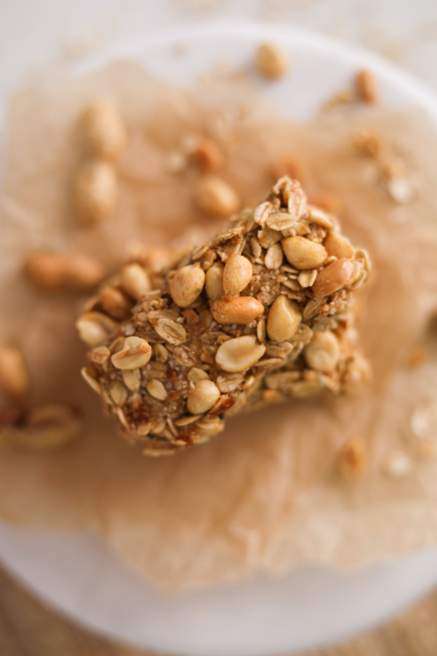 Top view of an oat bar topped with peanuts on a stack of bars surrounded by peanuts.
