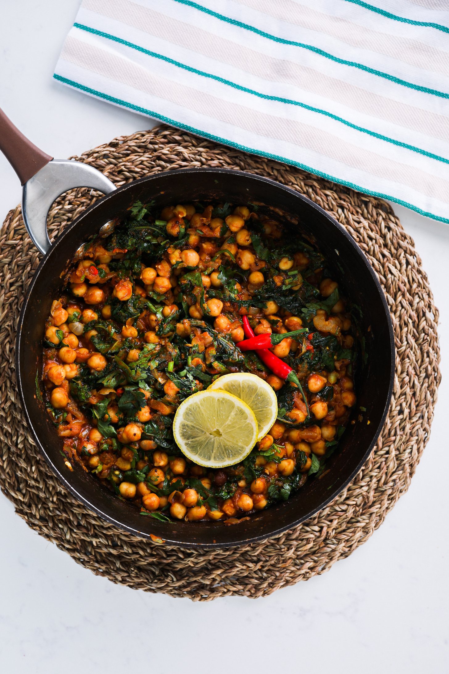 A pan of chickpea and greens curry topped with lemon slices and whole red chillies.