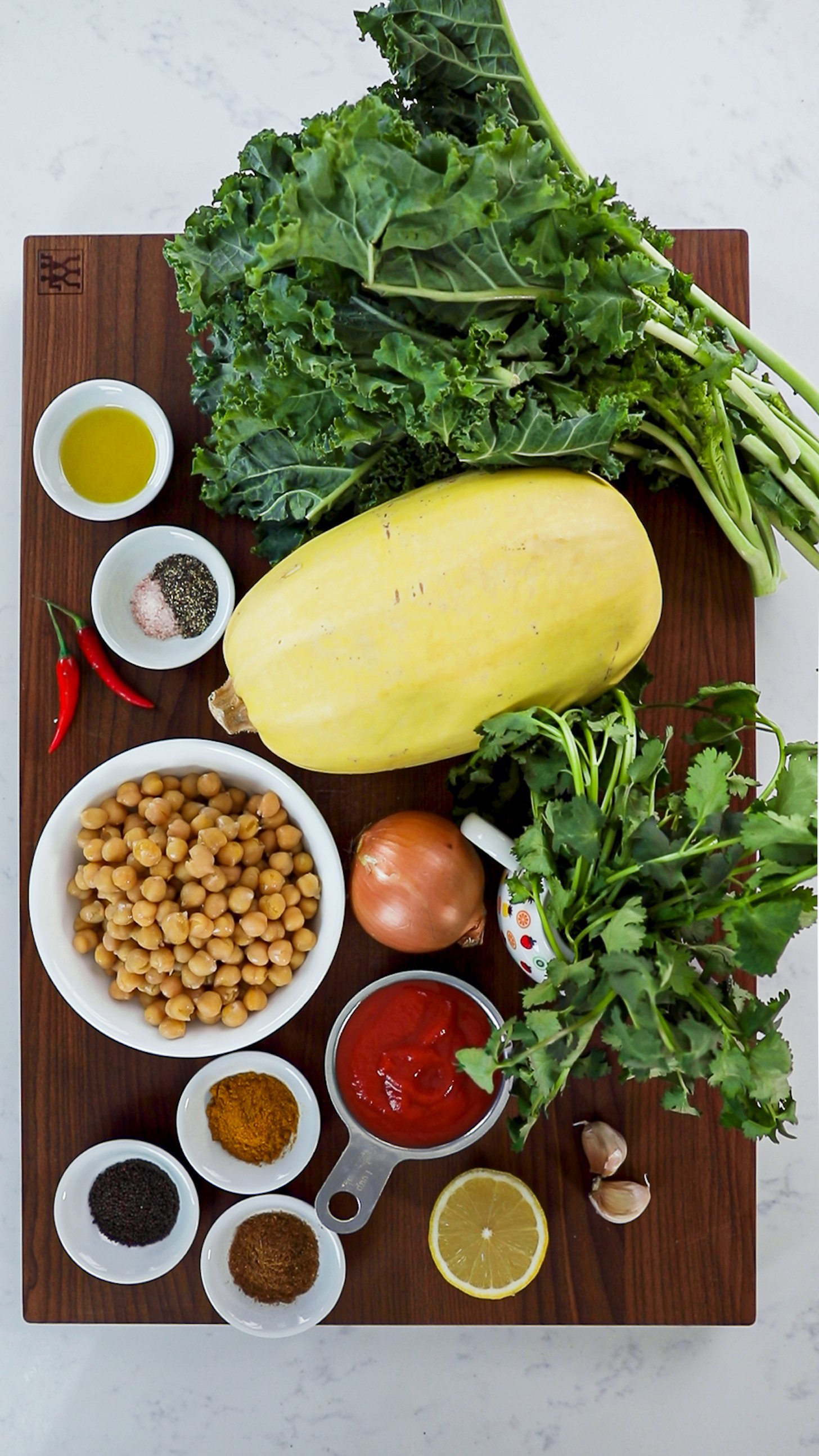 A collection of food ingredients including kale, spaghetti squash, chickpeas, herbs and spices in ramekins.