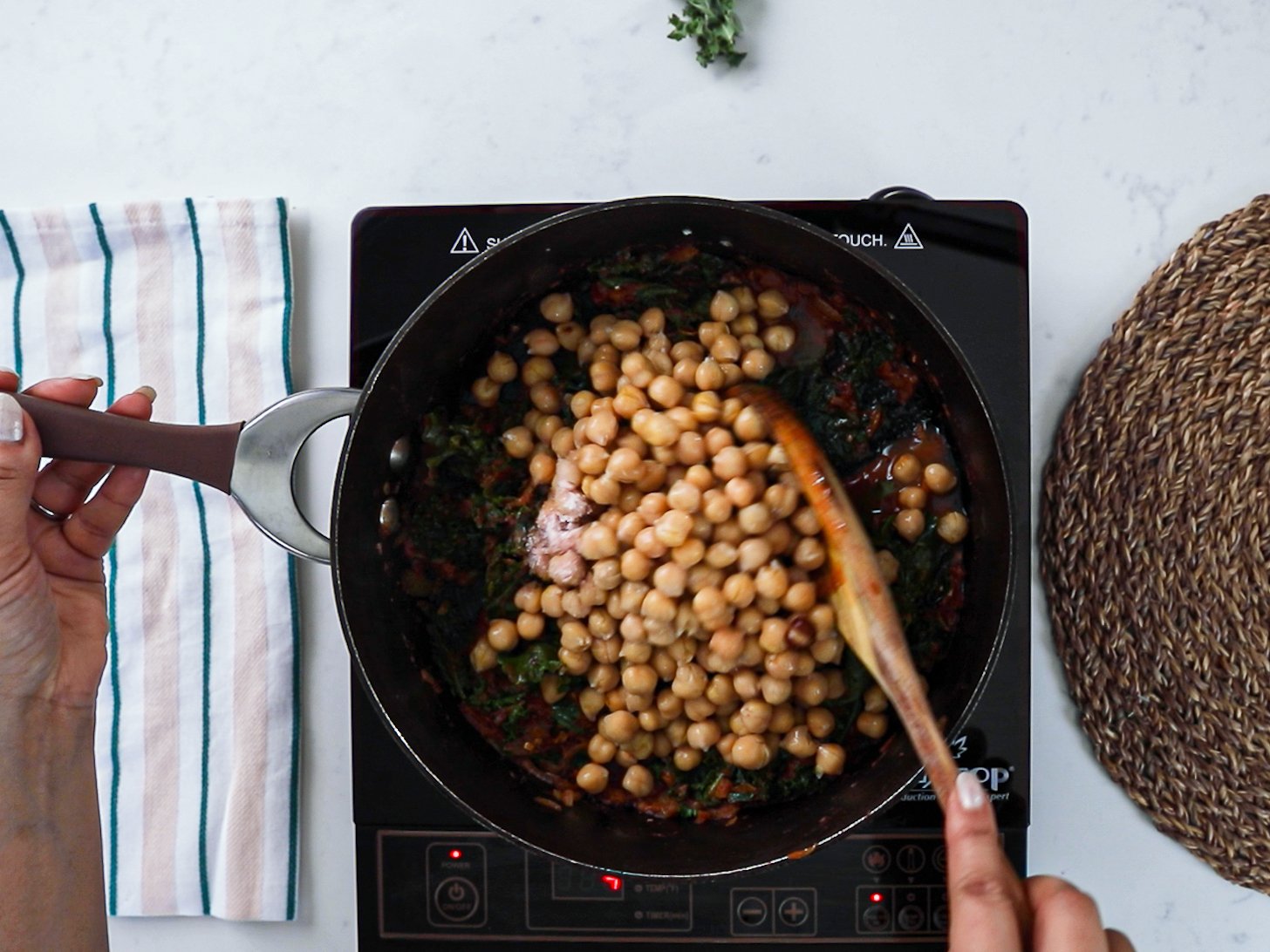 A hand stirring chickpeas in a pan.