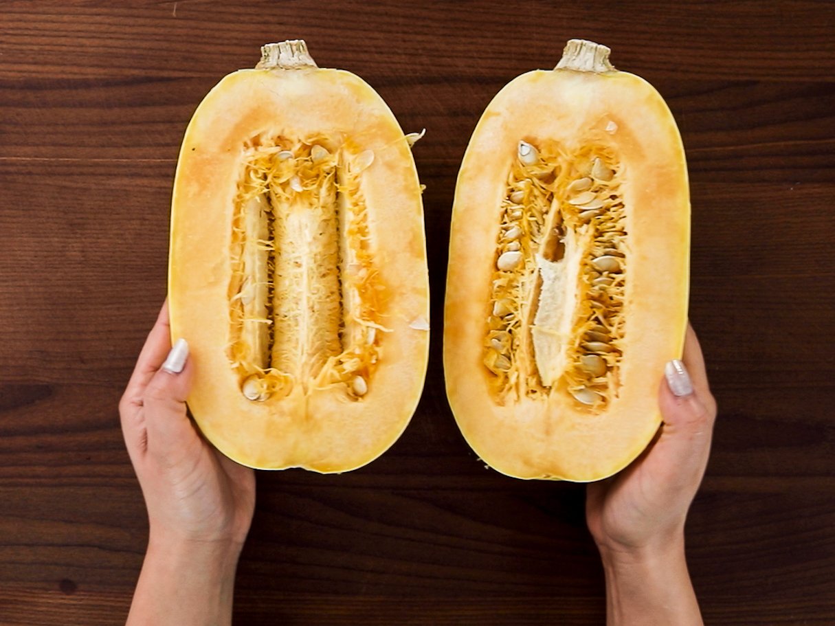 Hands holding two open halves of a spaghetti squash on a wooden chopping board.