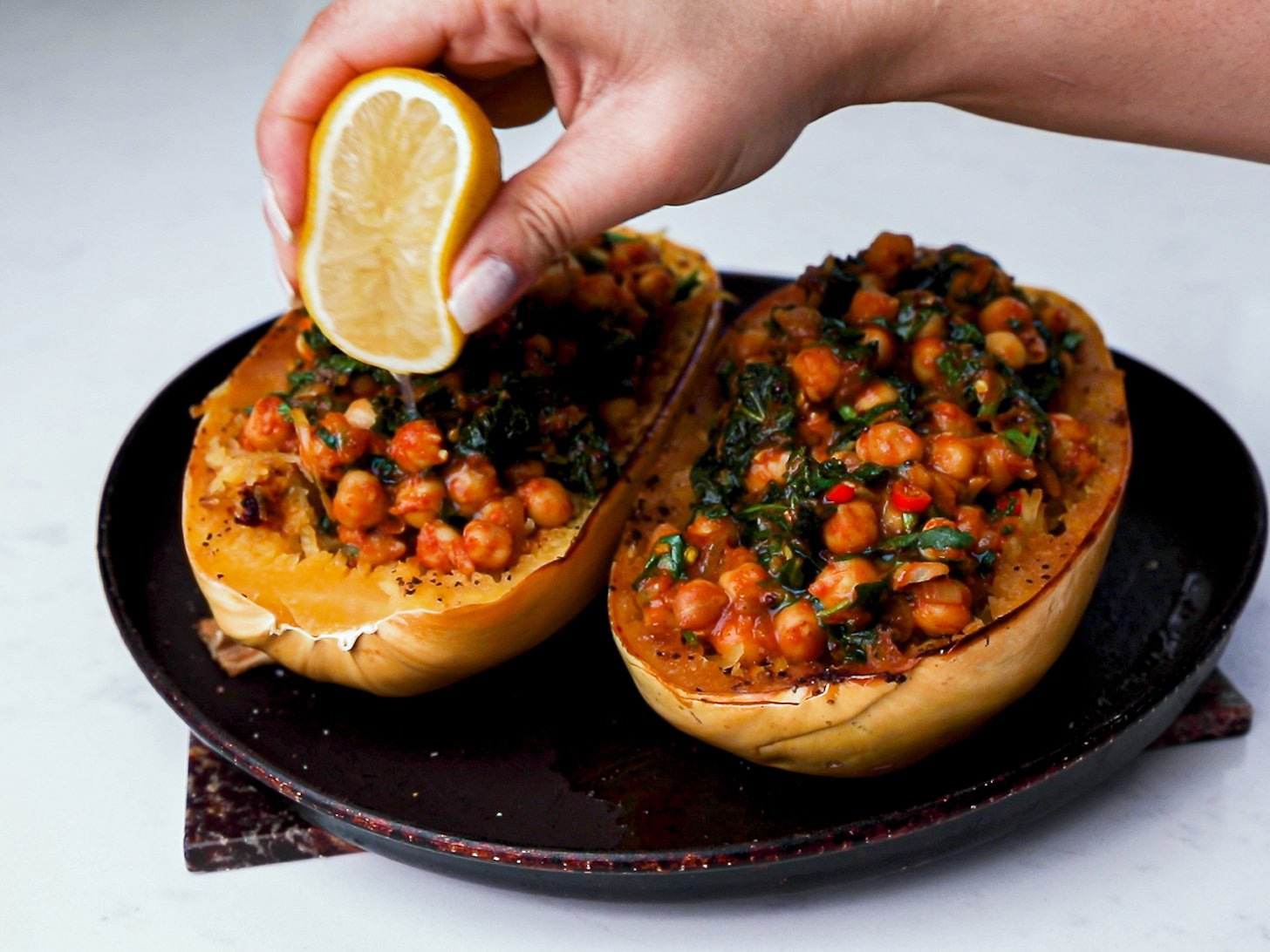A hand squeezing a lemon half over cooked spaghetti squash stuffed with chickpea curry.