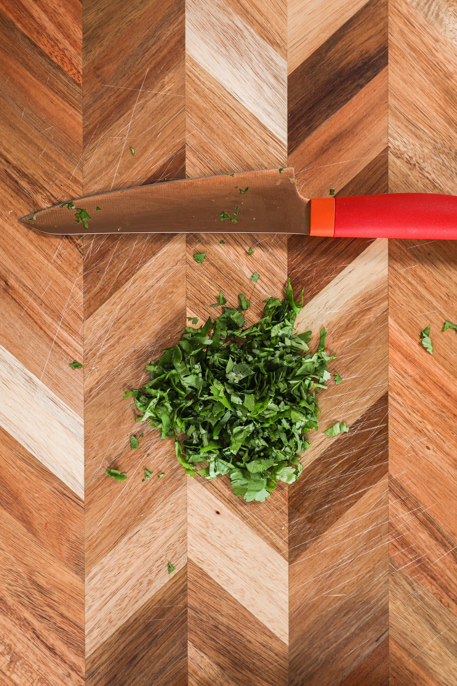 Finely chopped herbs and a knife on a chopping board.