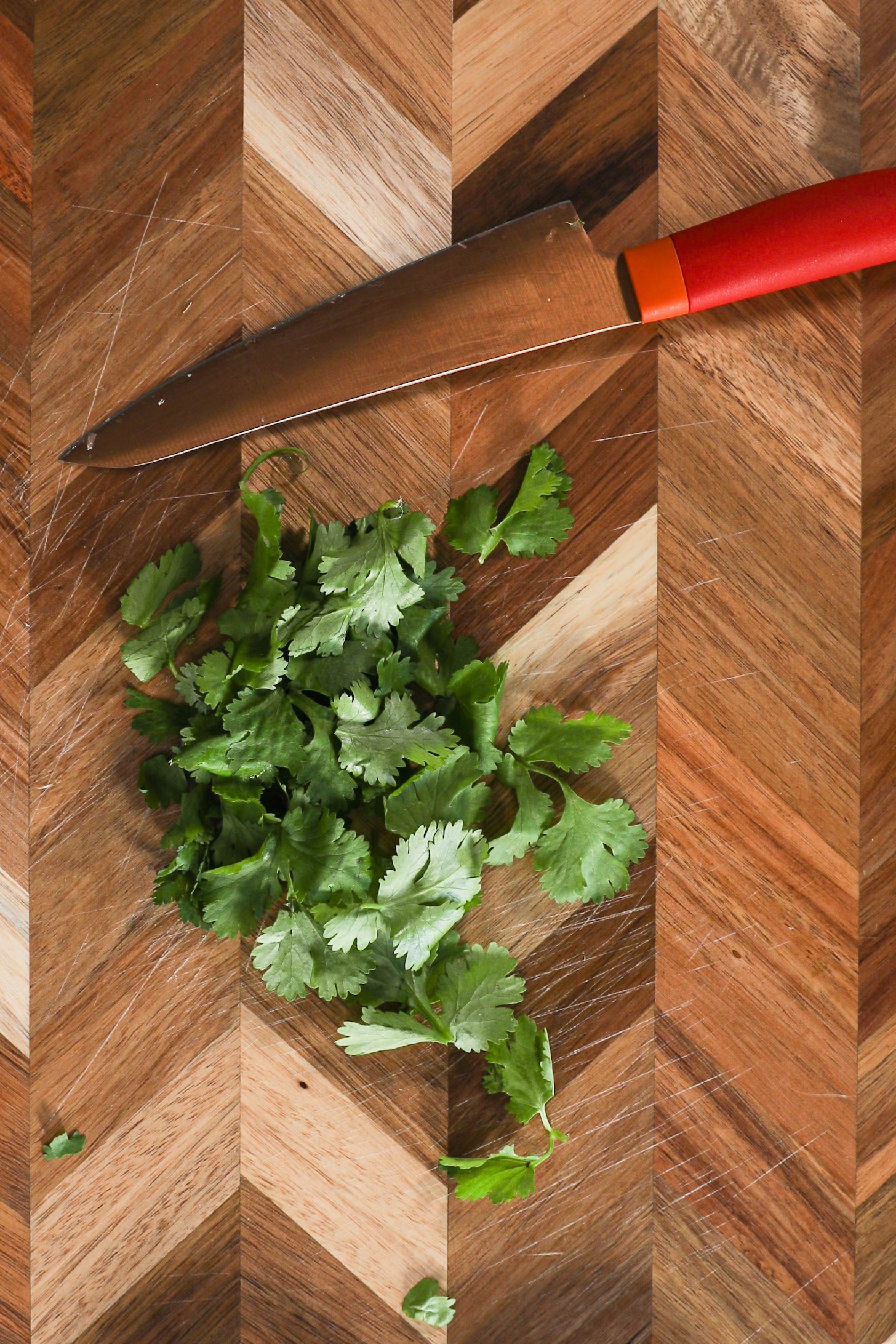 Cilantro leaves and a knife on a chopping board.