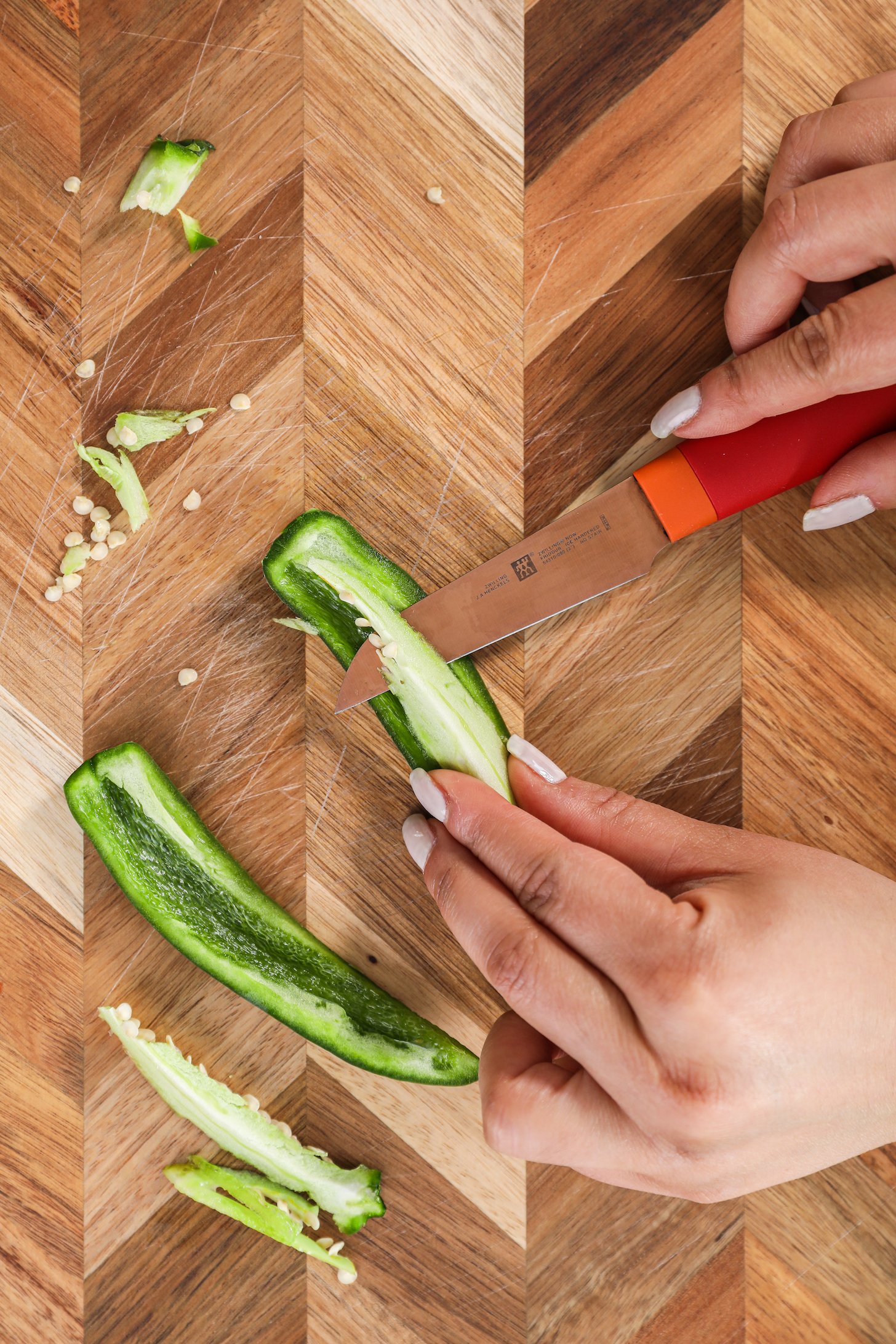 Hands holding a knife and cutting a jalapeno pepper.