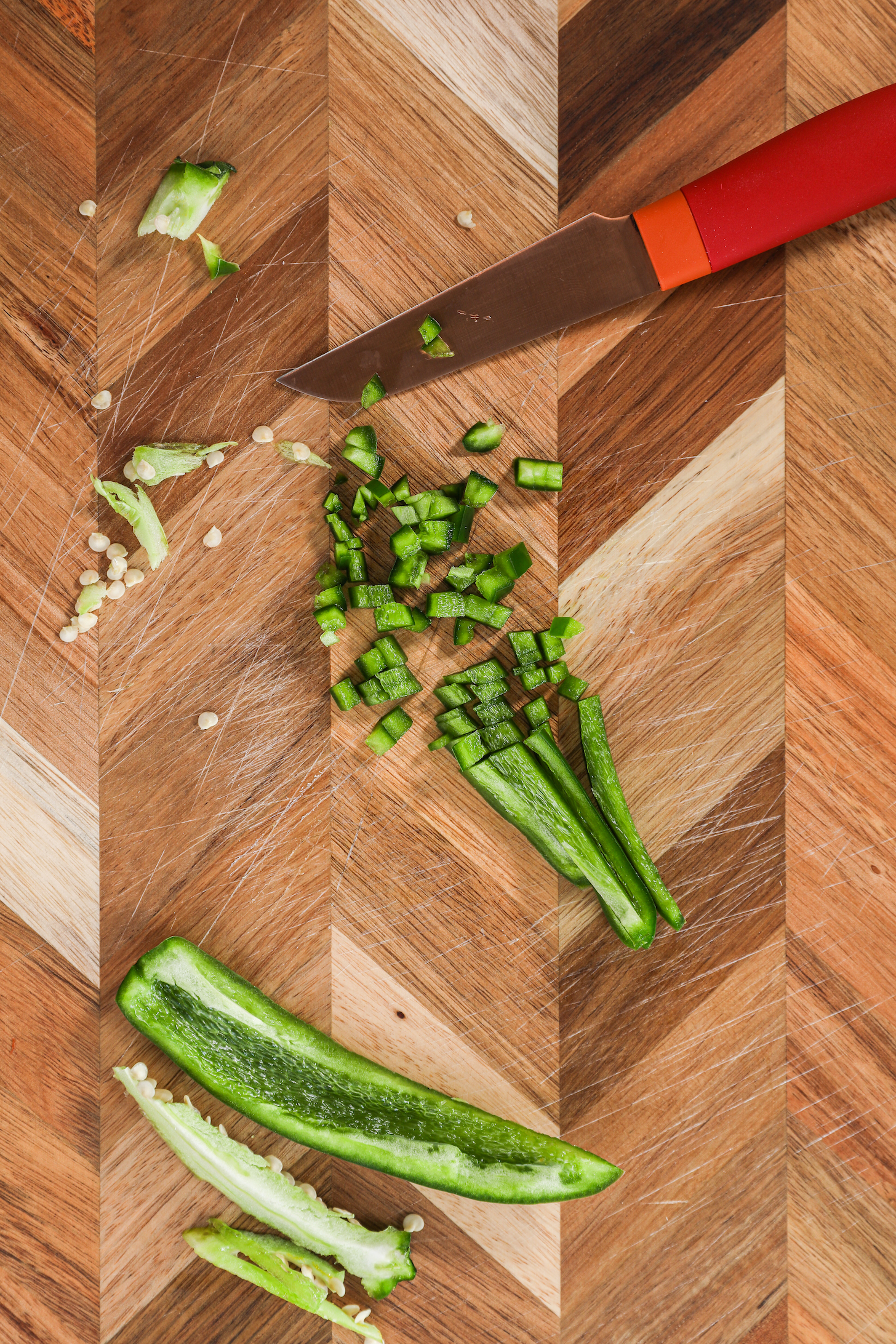 Chopped jalapeno pepper and a knife on a checkerboard style chopping board.