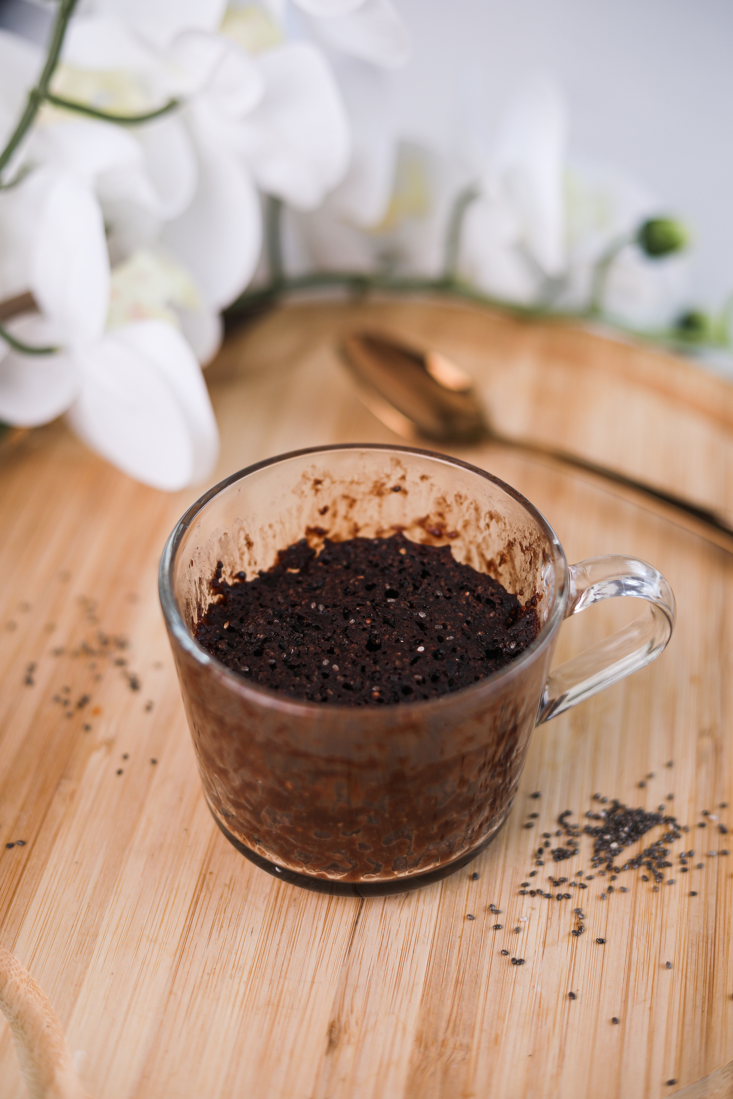 A perspective shot of a mug of chocolate cake with chia seeds around it and flowers in the background.