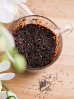 A mug containing chocolate cake with white flowers in the foreground.