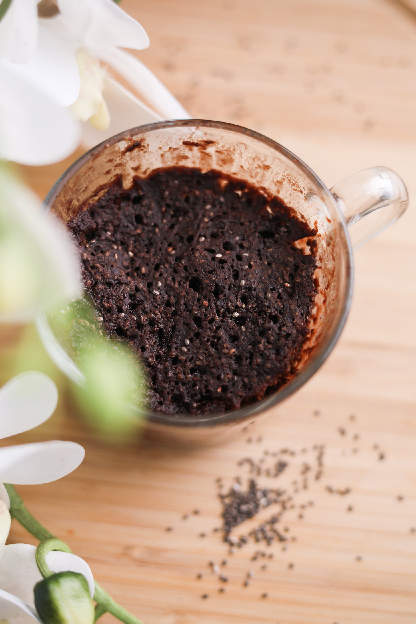 A mug containing chocolate cake with white flowers in the foreground.