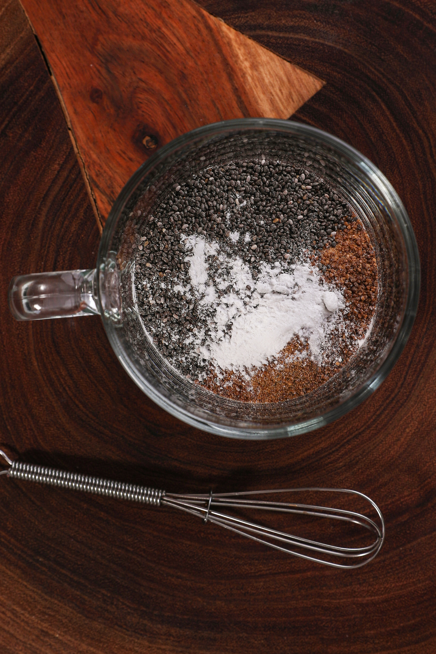A mug with seeds and cocoa as well as a white powder with a small whisk beside the mug.
