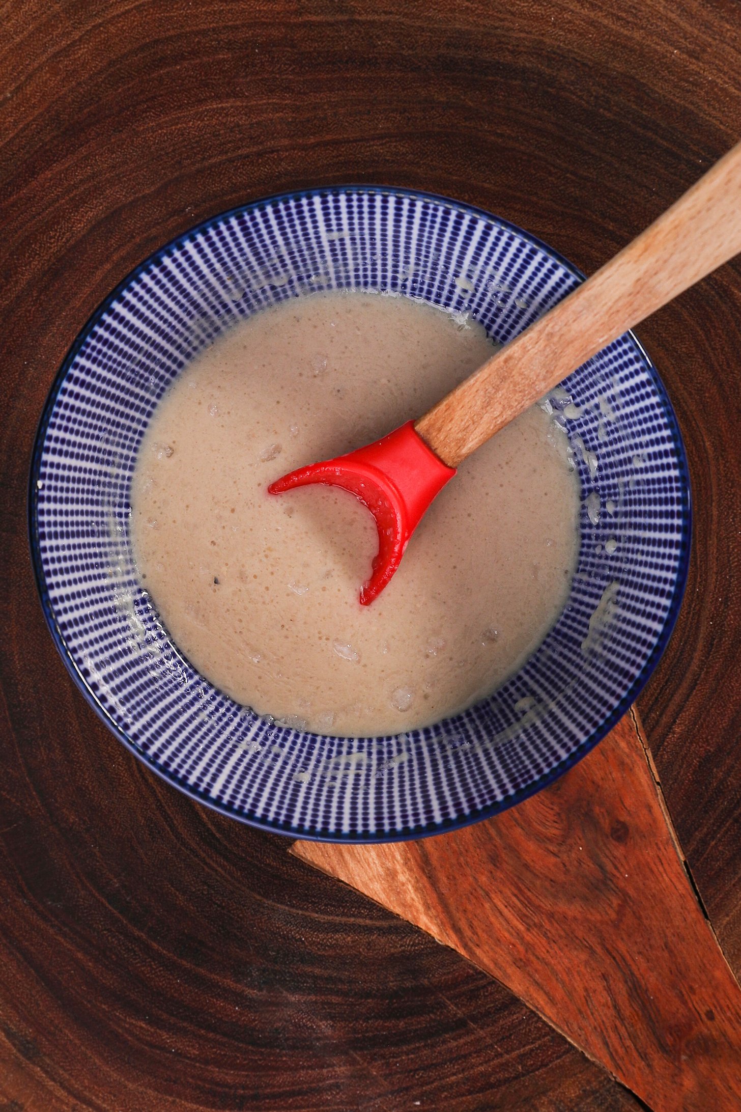 A blue bowl with stripes containing a beige liquid with a red spoon dipped in it.