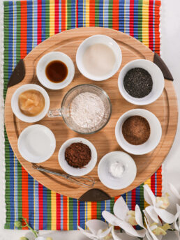 A collection of food ingredients like flour, milk, seeds, cacao displayed on a wooden board.