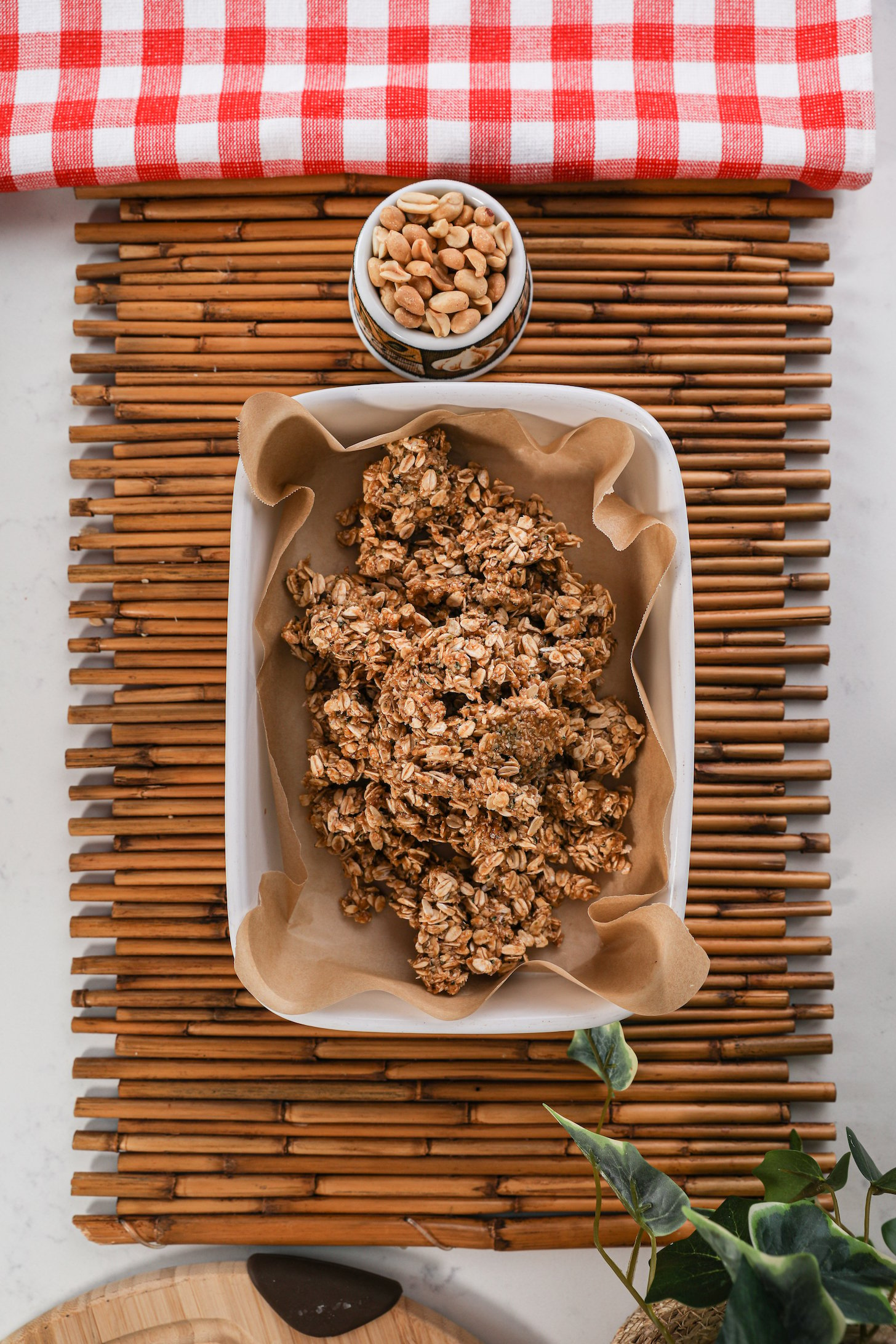A large chunk of rolled oats in a lined pan on a wooden mat with a ramekin of peanuts on the side.