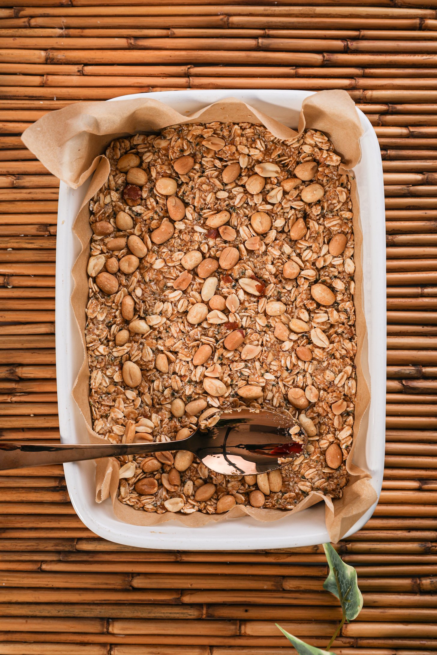 A pan of oats topped with whole peanuts with a gold spoon on top.