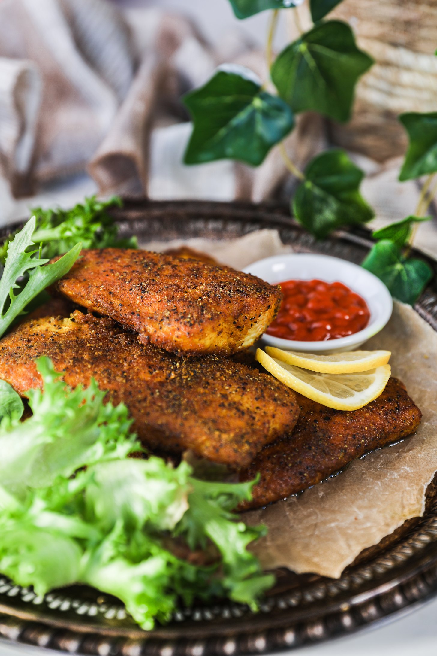 A pile of crispy fillets with lettuce and lemon slices on a tray with a plant in the background.