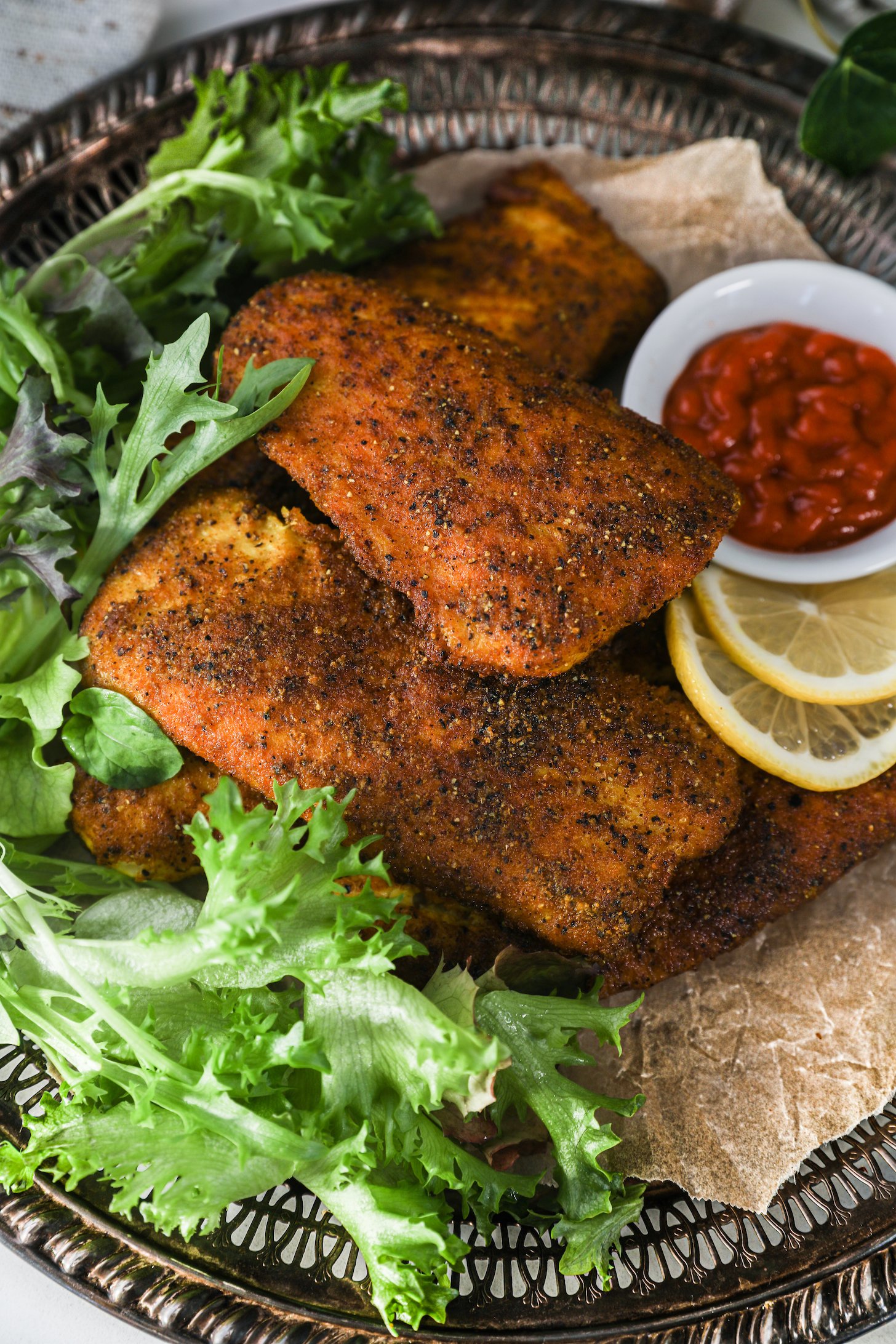 Perspective view of a pile of crispy fillets with lettuce and lemon slices on a tray.