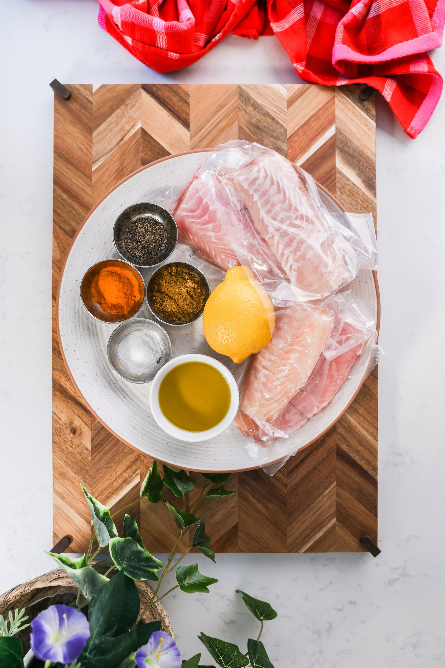 A collection of ingredients including white fish fillets, spices, oil and lemon.