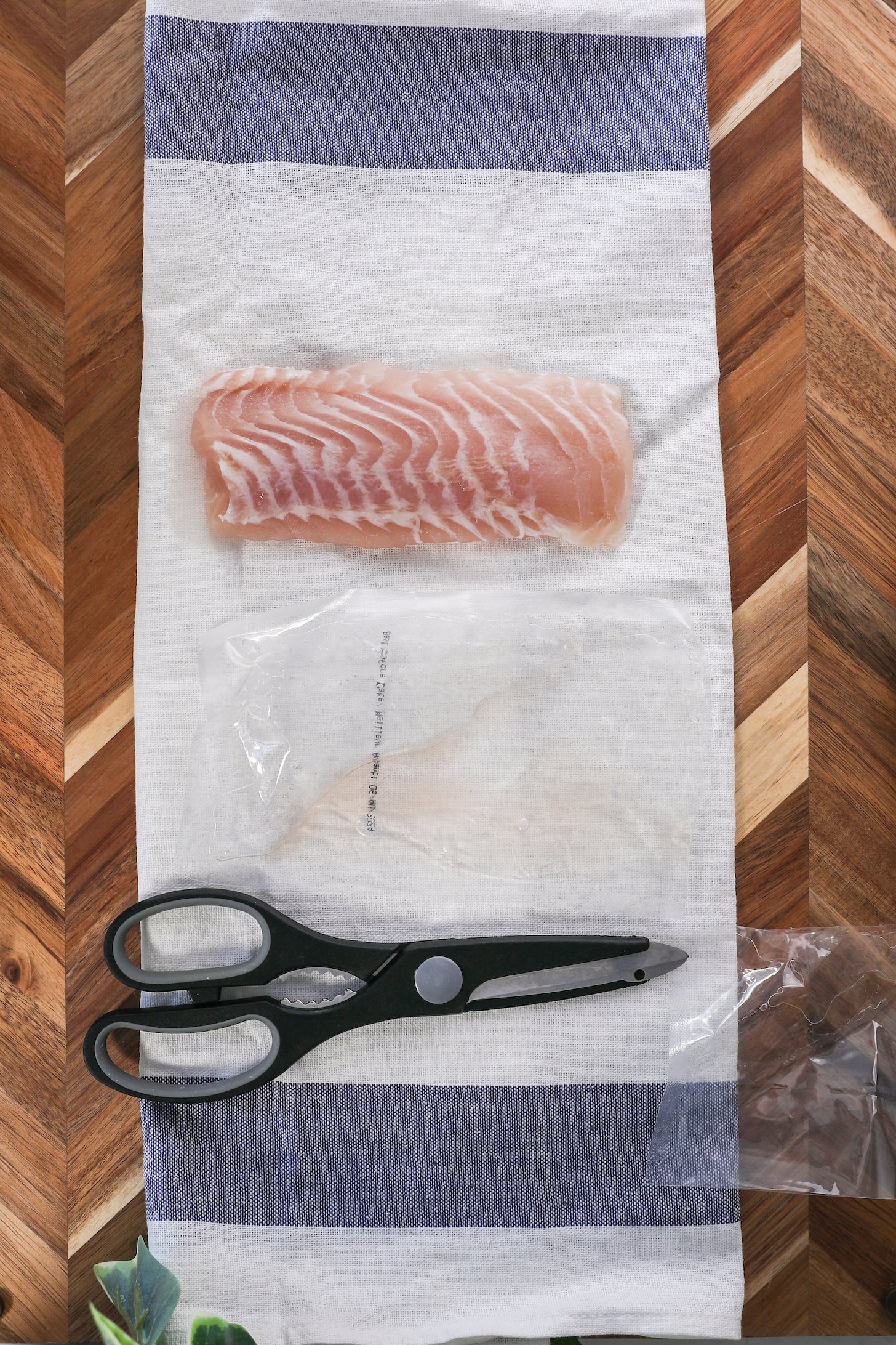 A white fish fillet on a t-towel with a pair of black scissors next to it.
