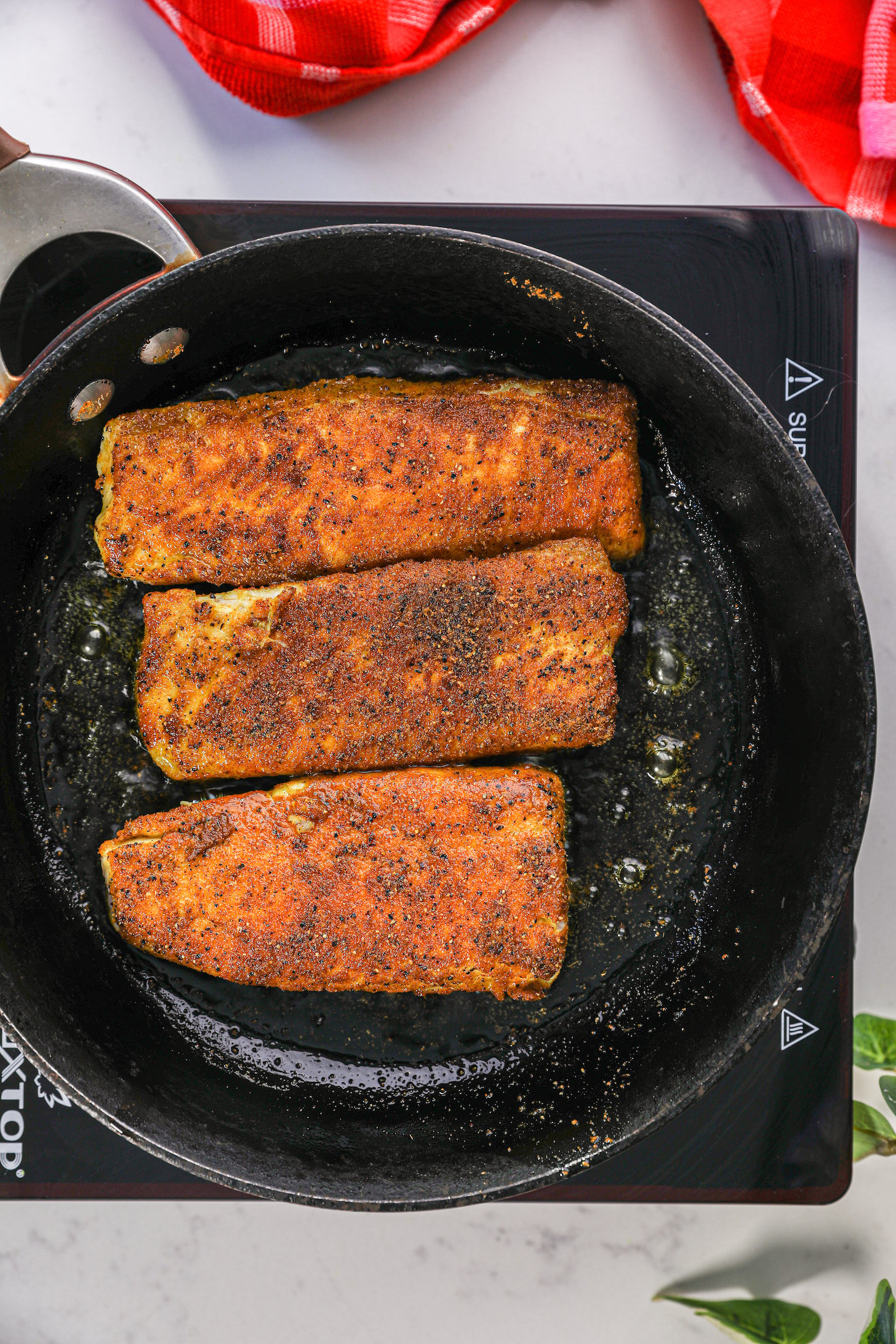 Three spice-coated fish fillets frying in a pan of oil.