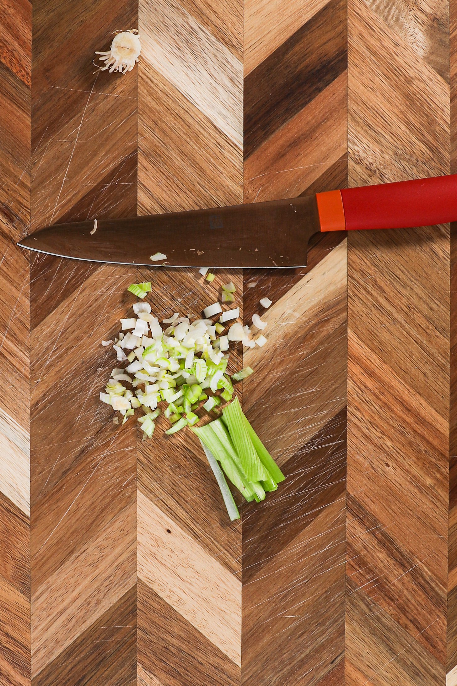 Strips of spring onion chopped finely with a red knife on a checkered wooden board.