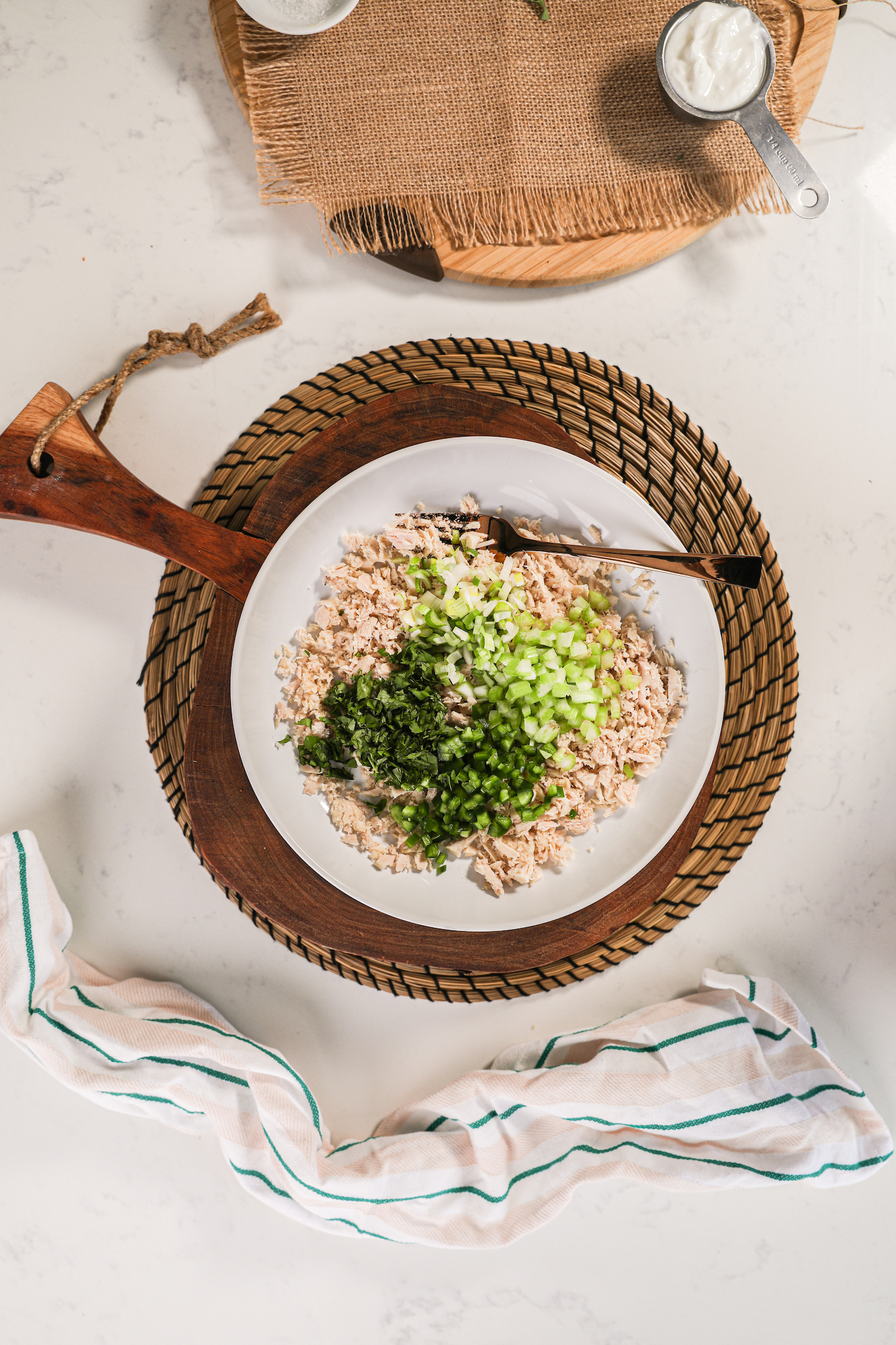A birdseye view of a bowl of shredded fish topped with chopped celery and herbs.