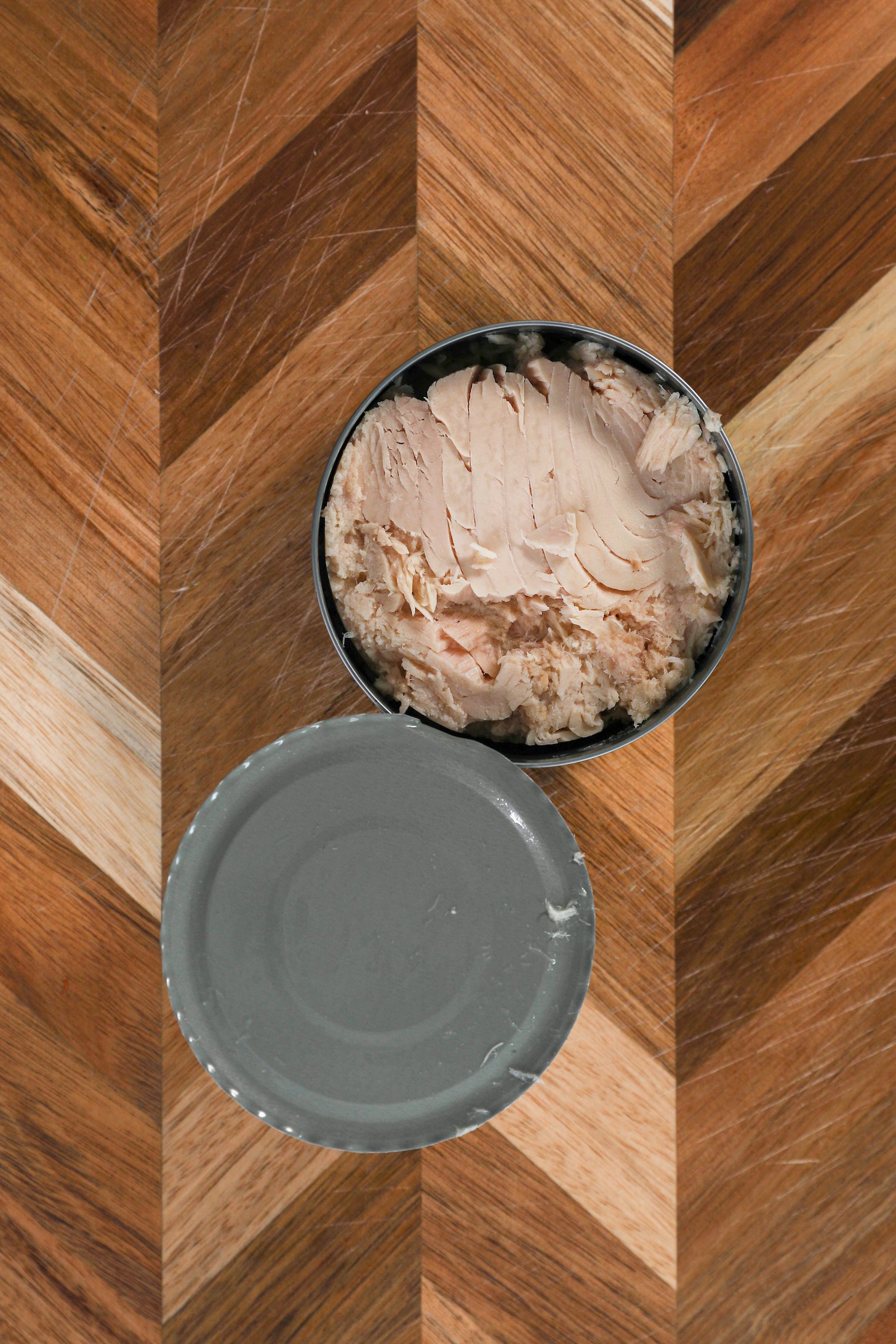 A open can of drained tuna fish on a wooden board.