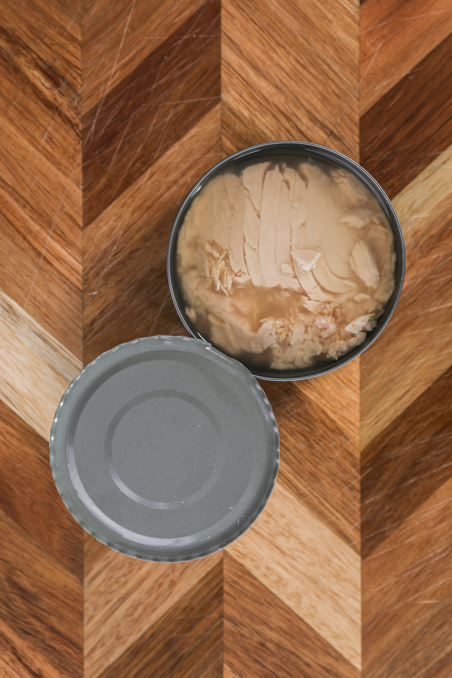 A open can of tuna fish in water on a wooden board.
