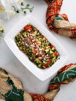 A rectangular bowl filled with chopped vegetables, beans and topped with almonds, styled around a decorative scarf.