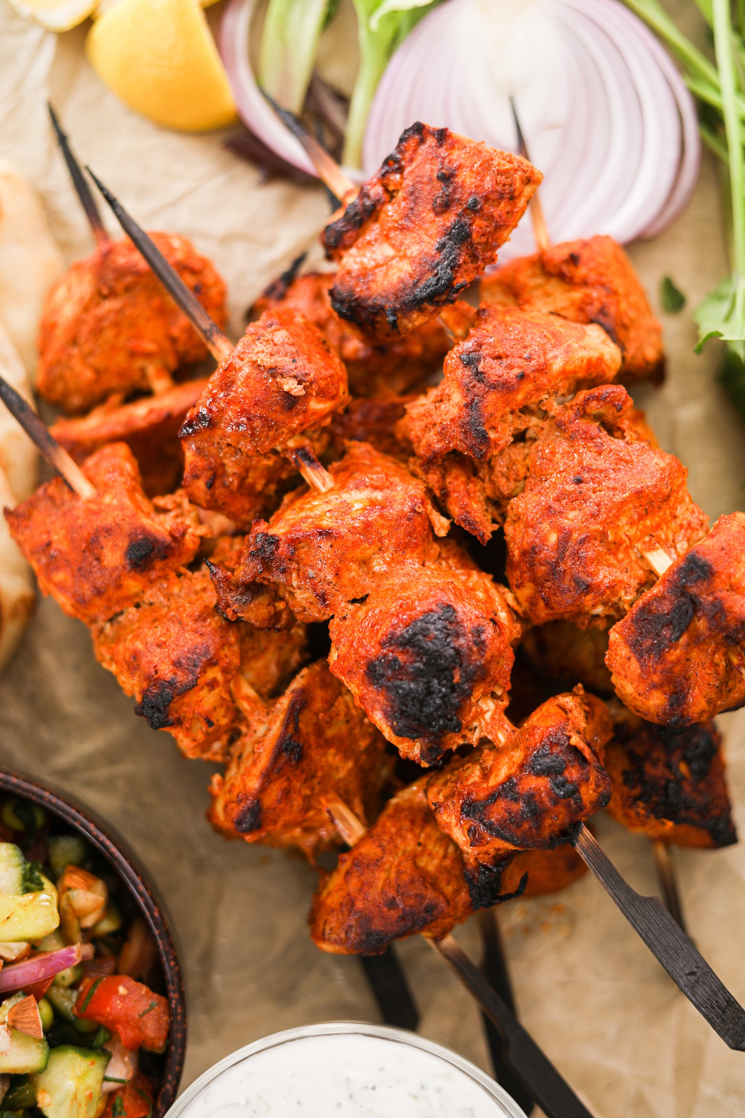 Perspective shot of a pile of chicken skewers with lemon in the background.