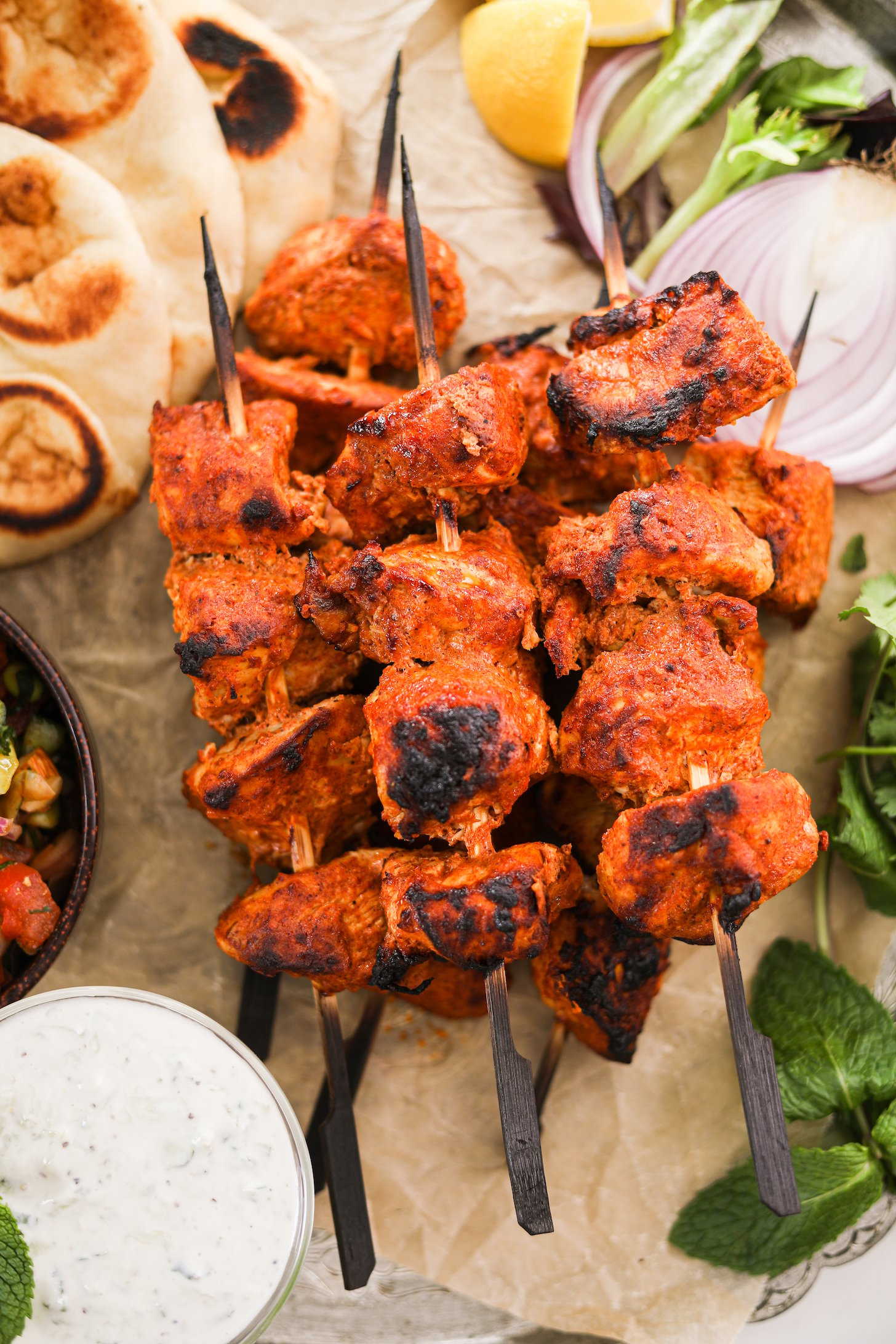 A pile of chicken skewers with naan and lemon in the background.