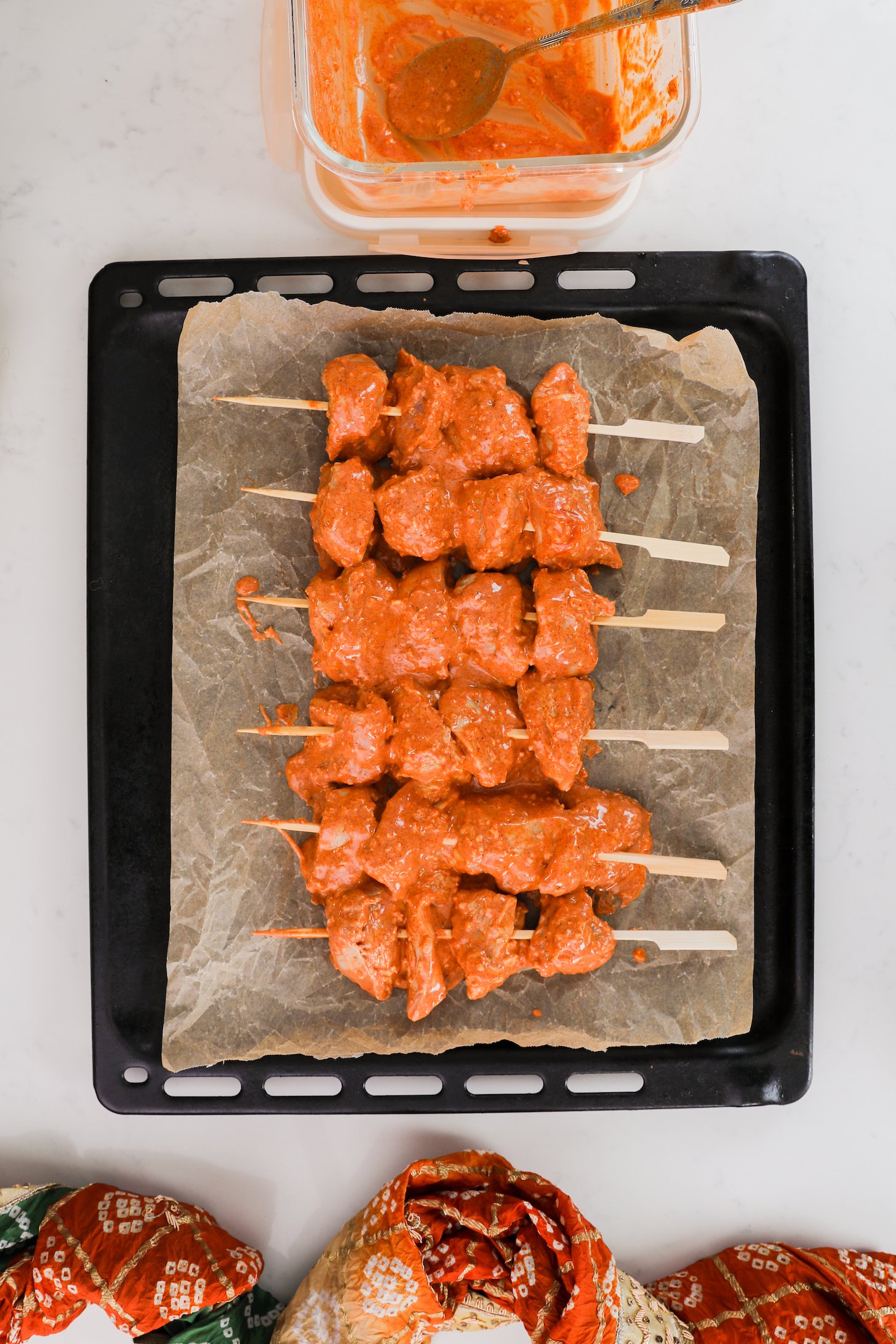 Skewers of orange-coloured chicken on a black tray,