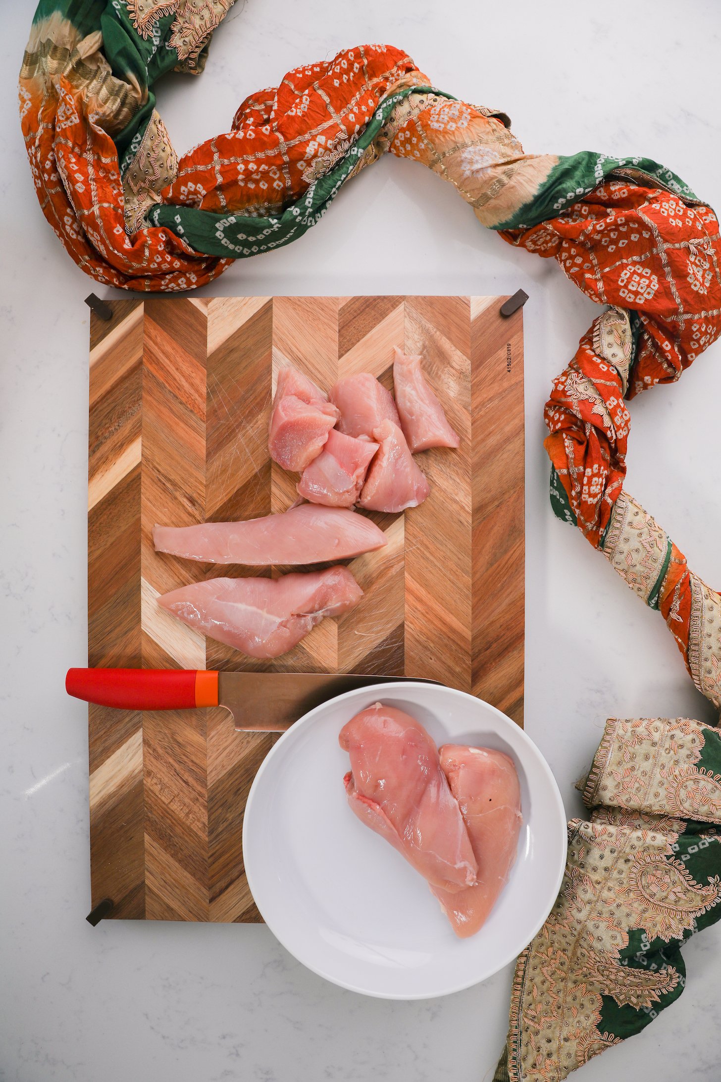 Chicken breast on a wooden board with a knife styled with a decorative scarf.