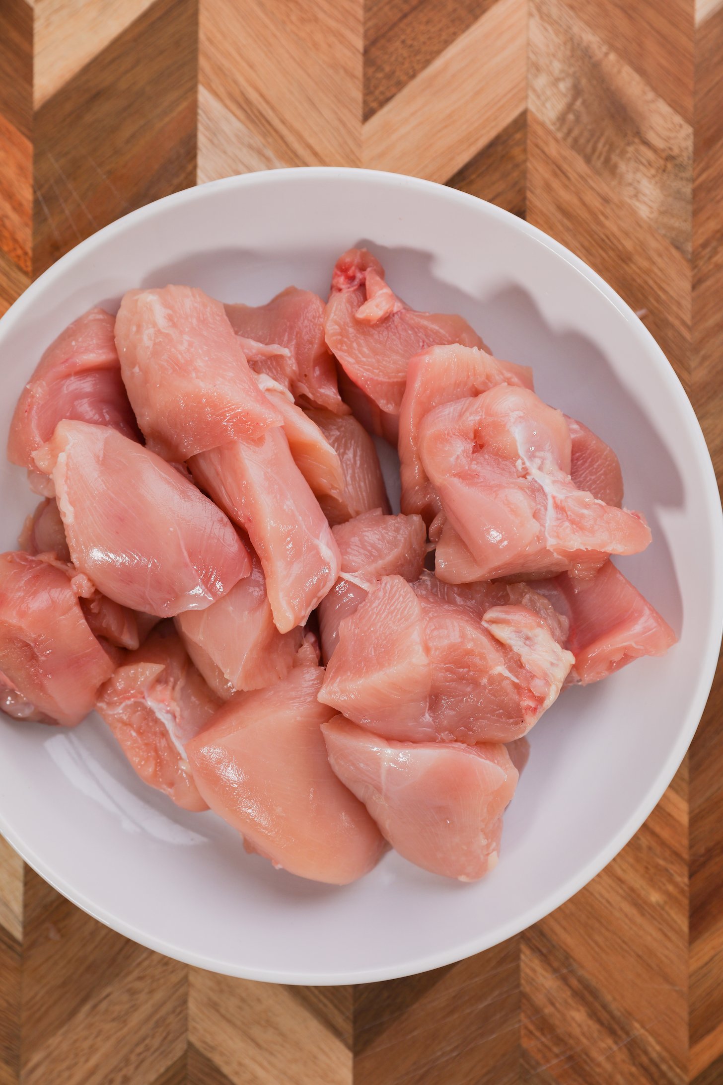 A bowl of chicken pieces on a wooden board.