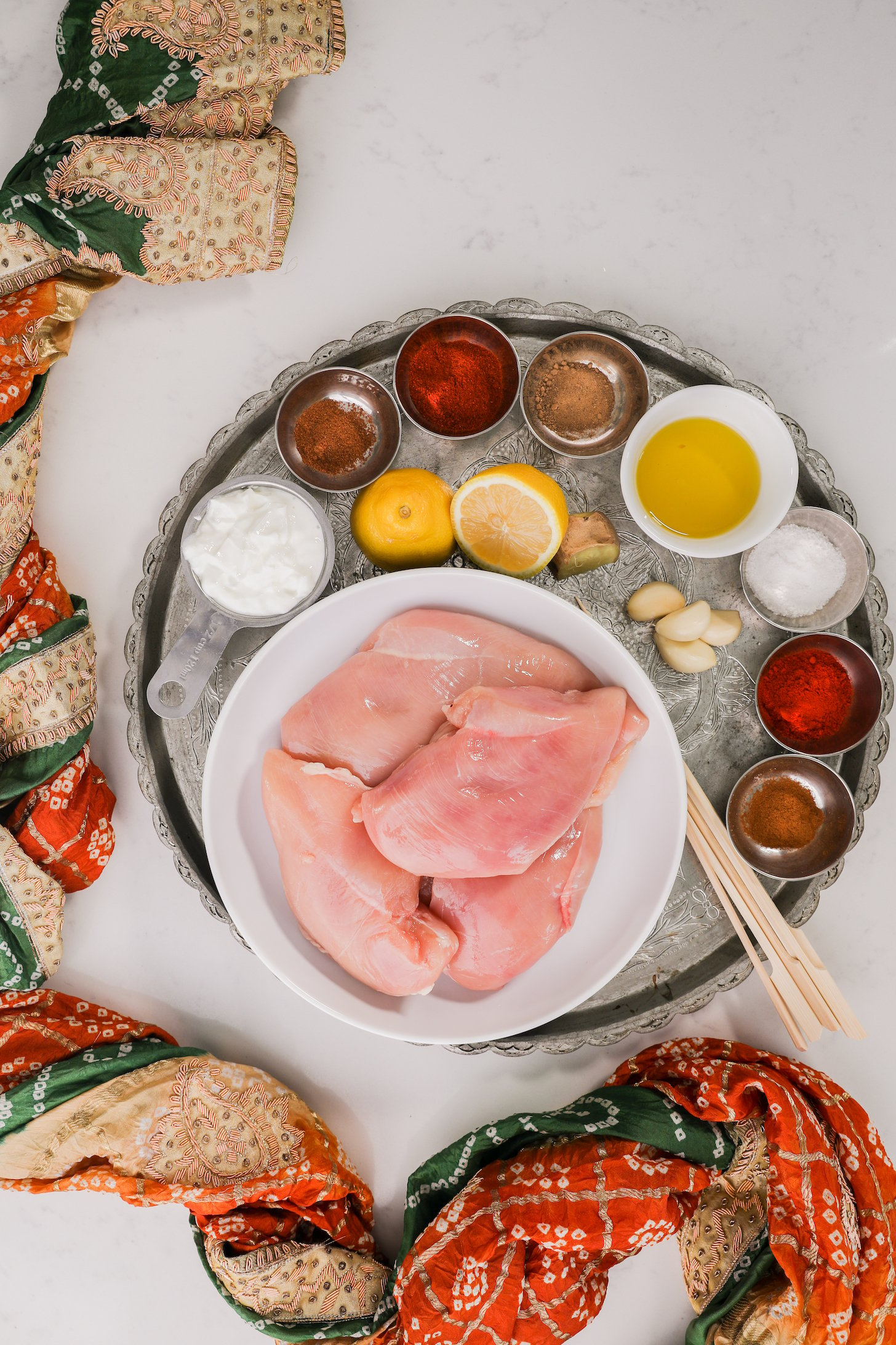 A collection of food ingredients like chicken spices, lemon and yogurt styled on a silver tray.