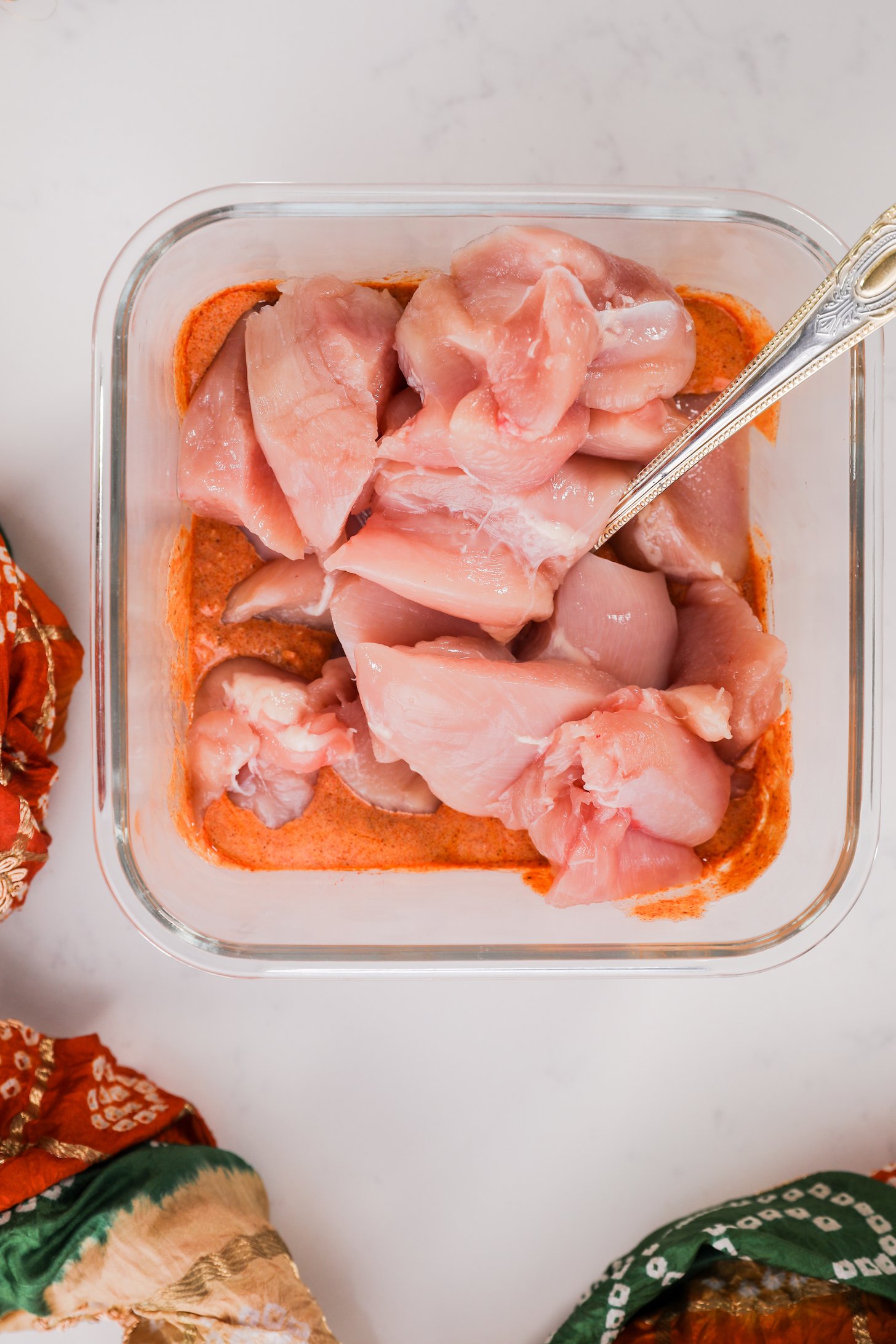 Chunks of chicken in a square glass container with an orange sauce.