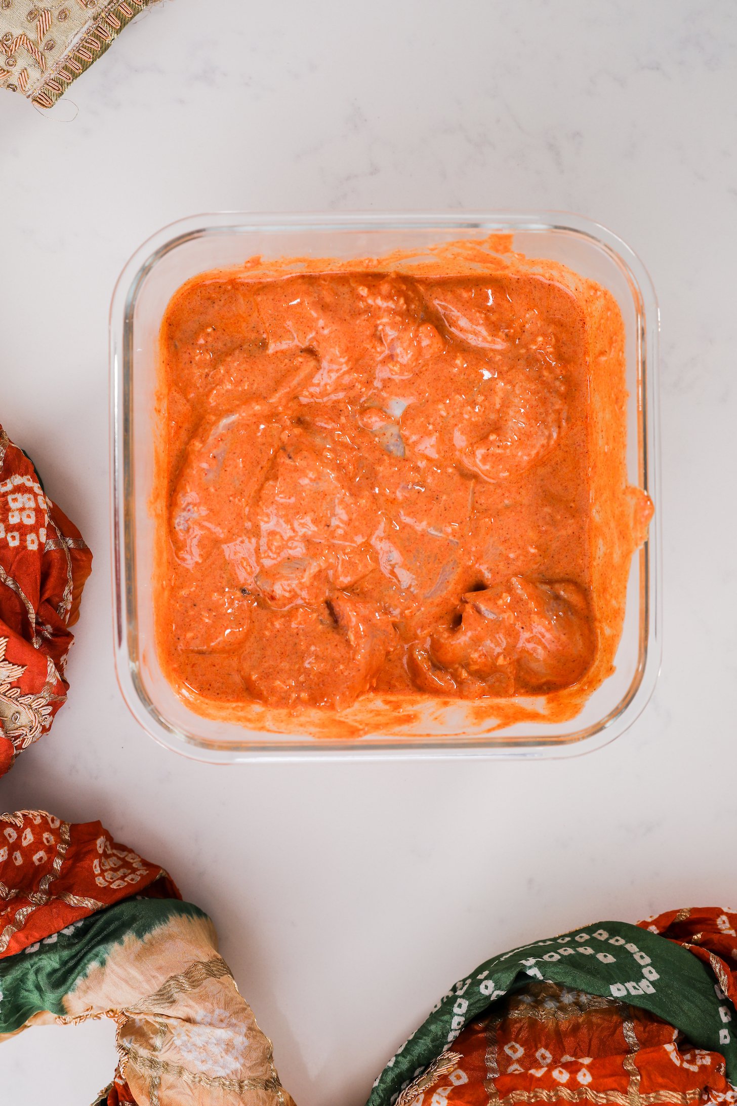 A square glass container with meat in an orange sauce, styled with a decorative scarf.