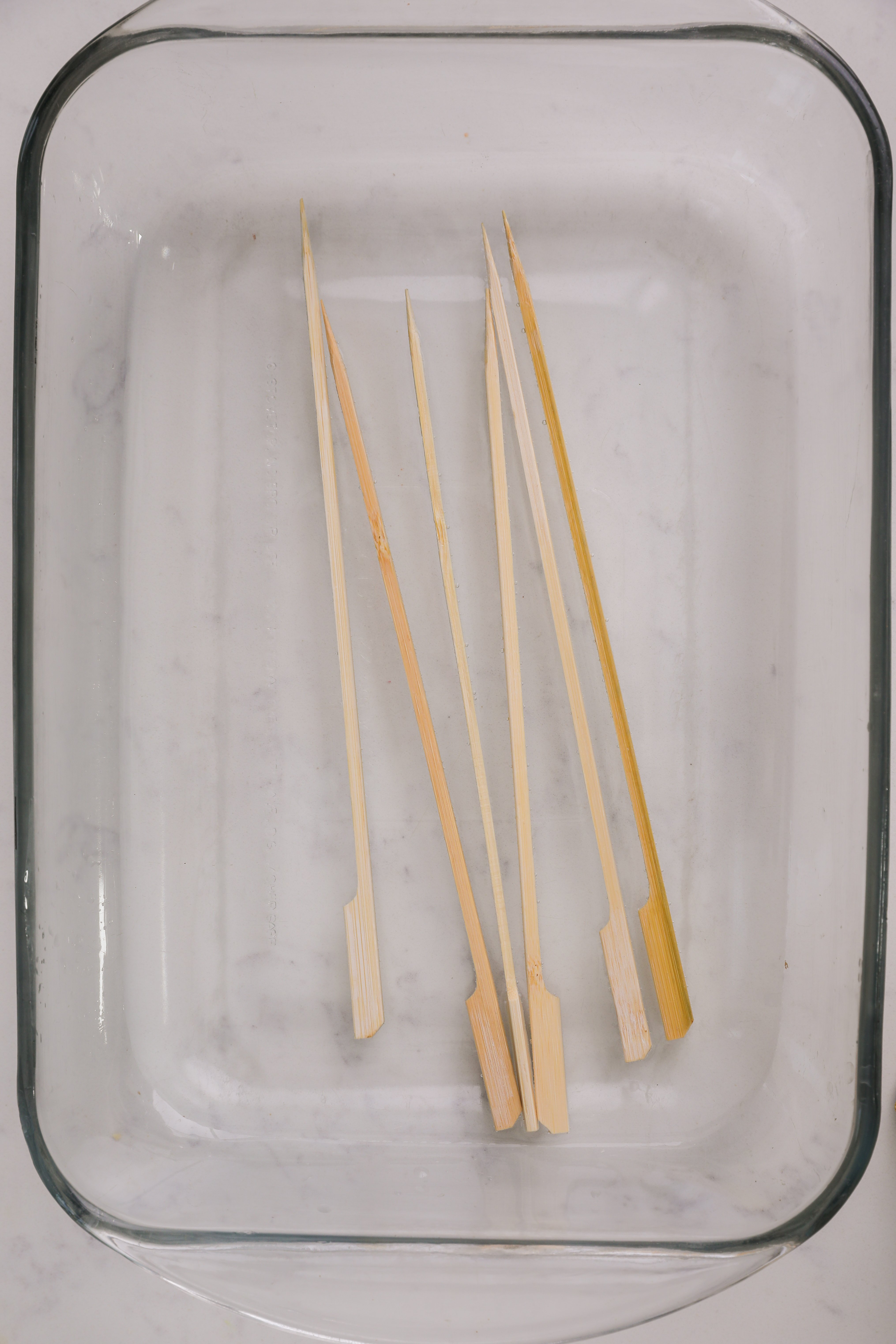 Six wooden skewers in a large glass dish.
