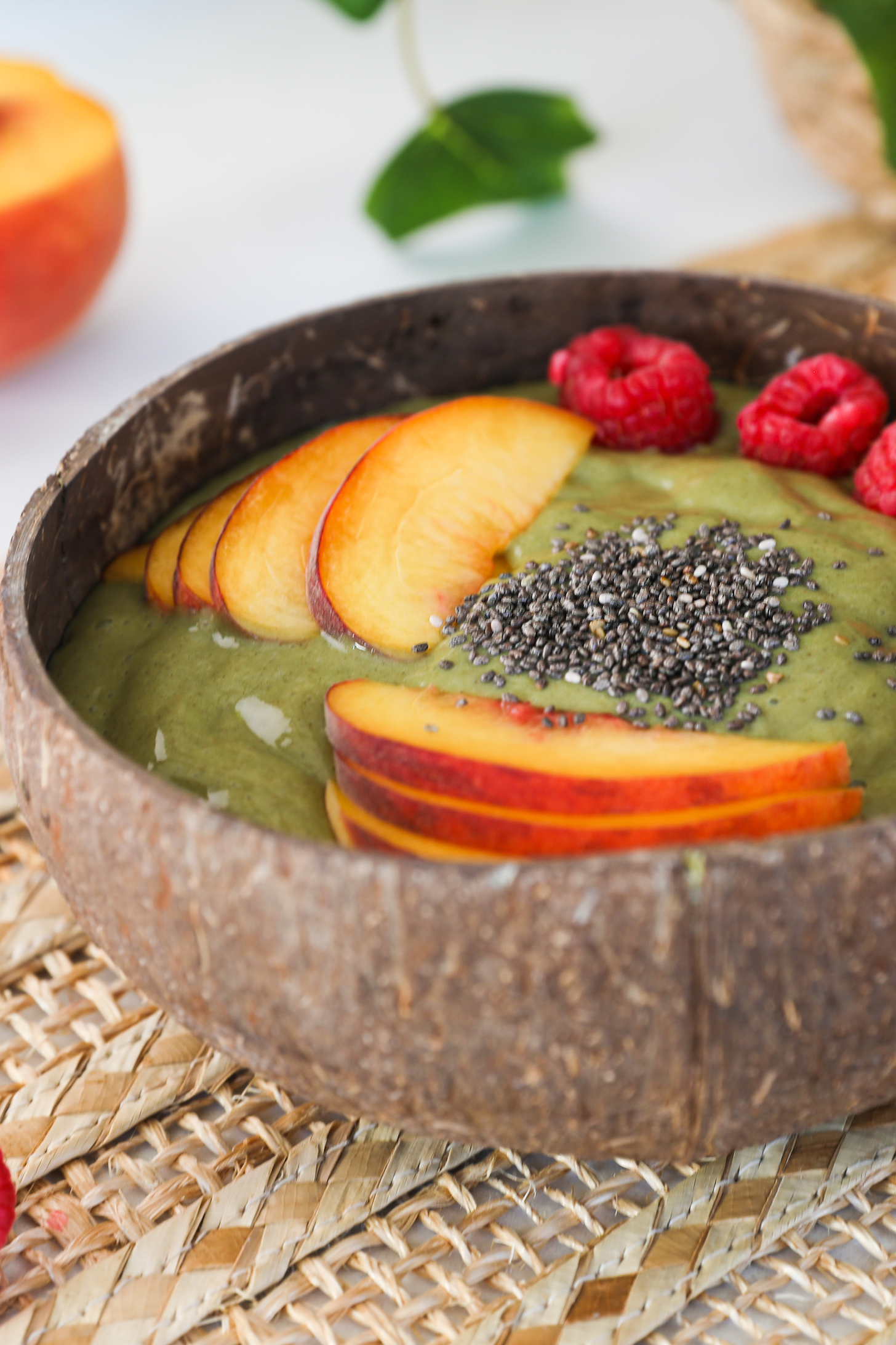 Perspective shot of a coconut bowl of green smoothie topped with fruit and chia seeds.