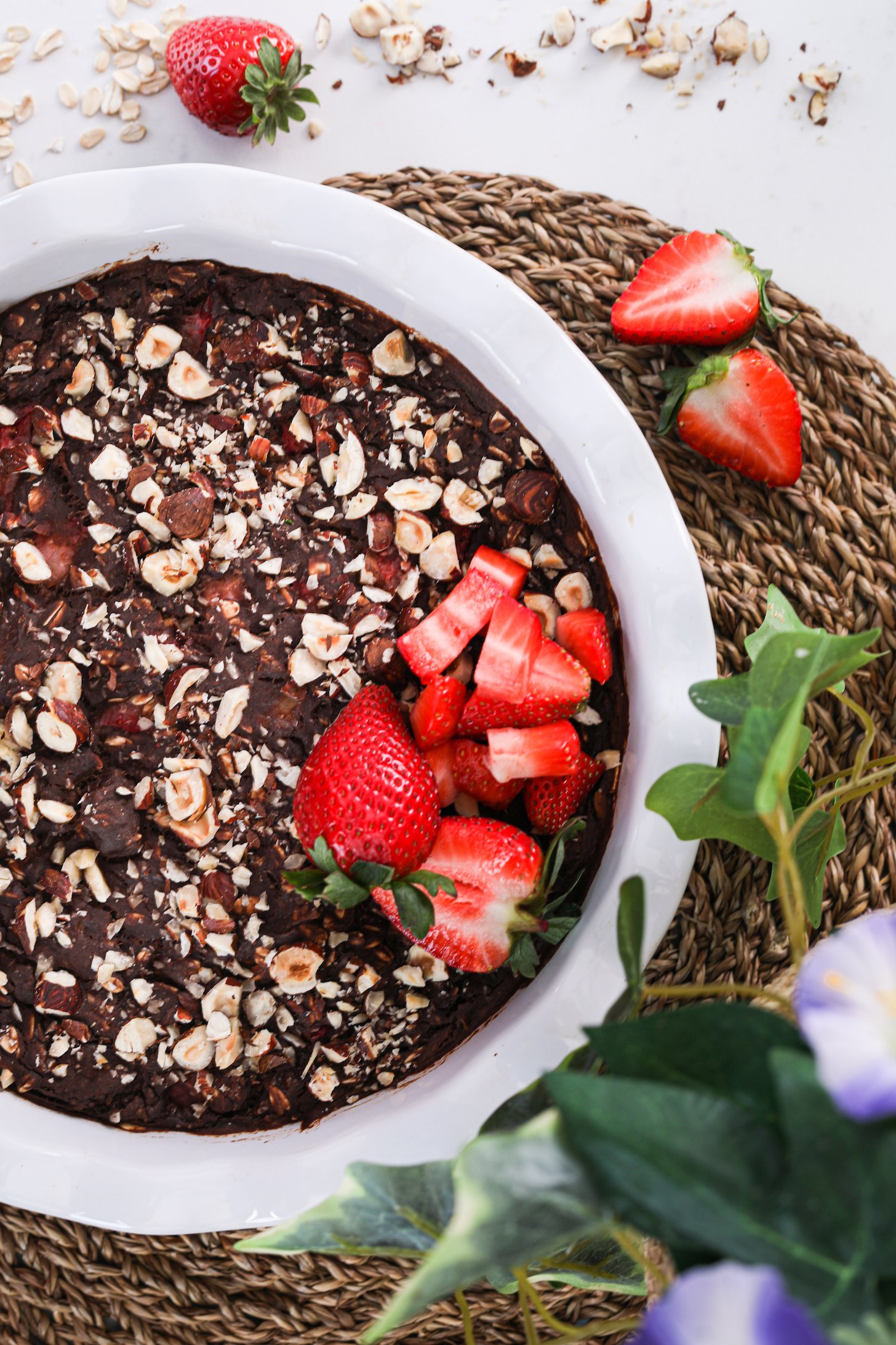 Top view of a bowl of chocolate dessert topped with nuts and a small pile of strawberries on one side.