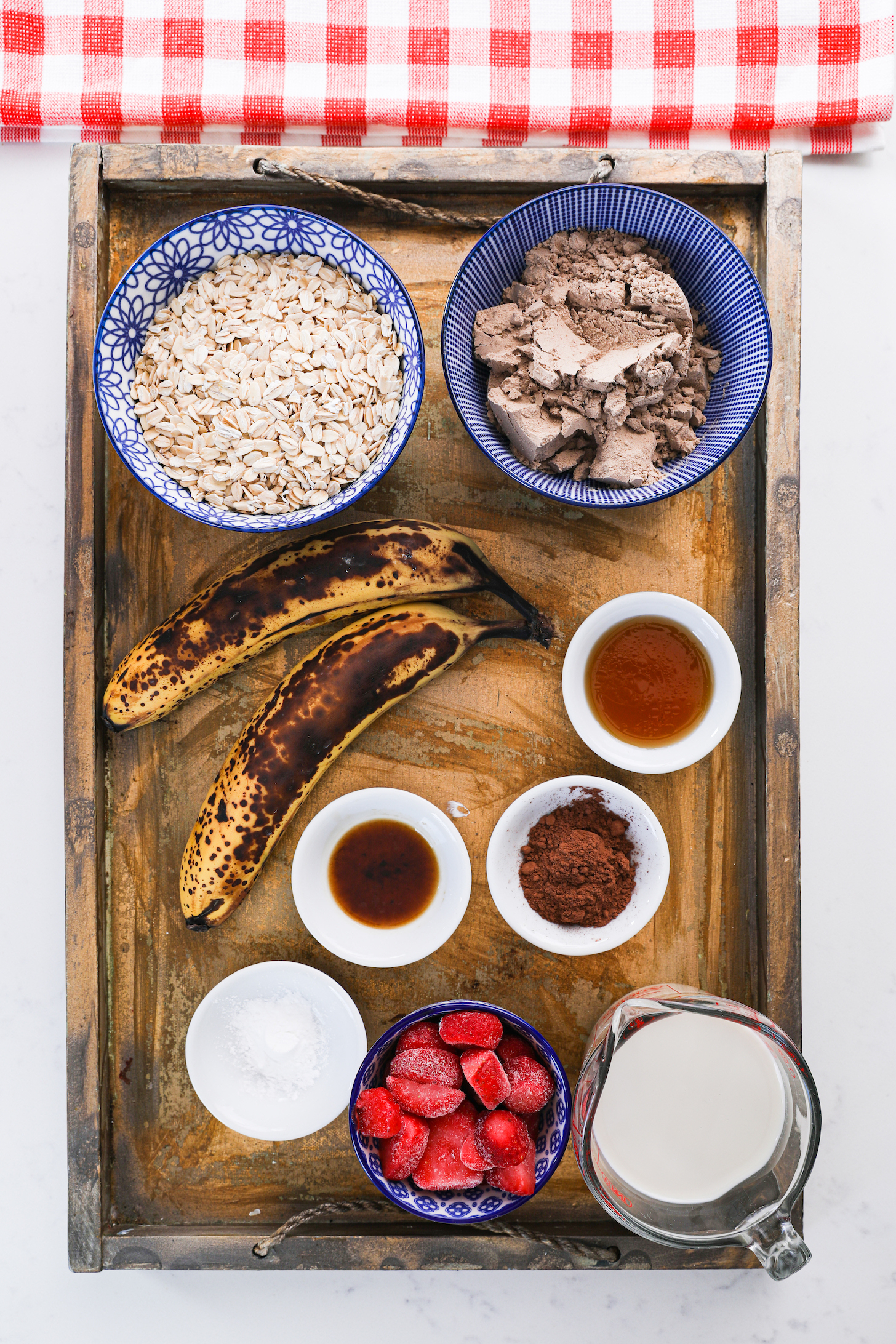 Food ingredients like bananas, oats, strawberries and millk arranged in a gold tray.
