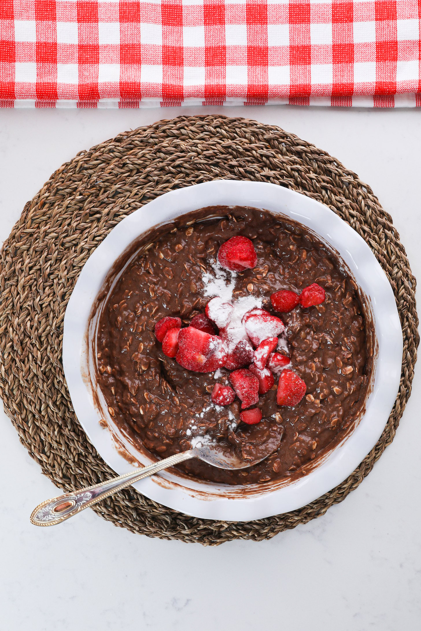 Bowl of chocolate oats topped with frozen strawberries and a white powder.