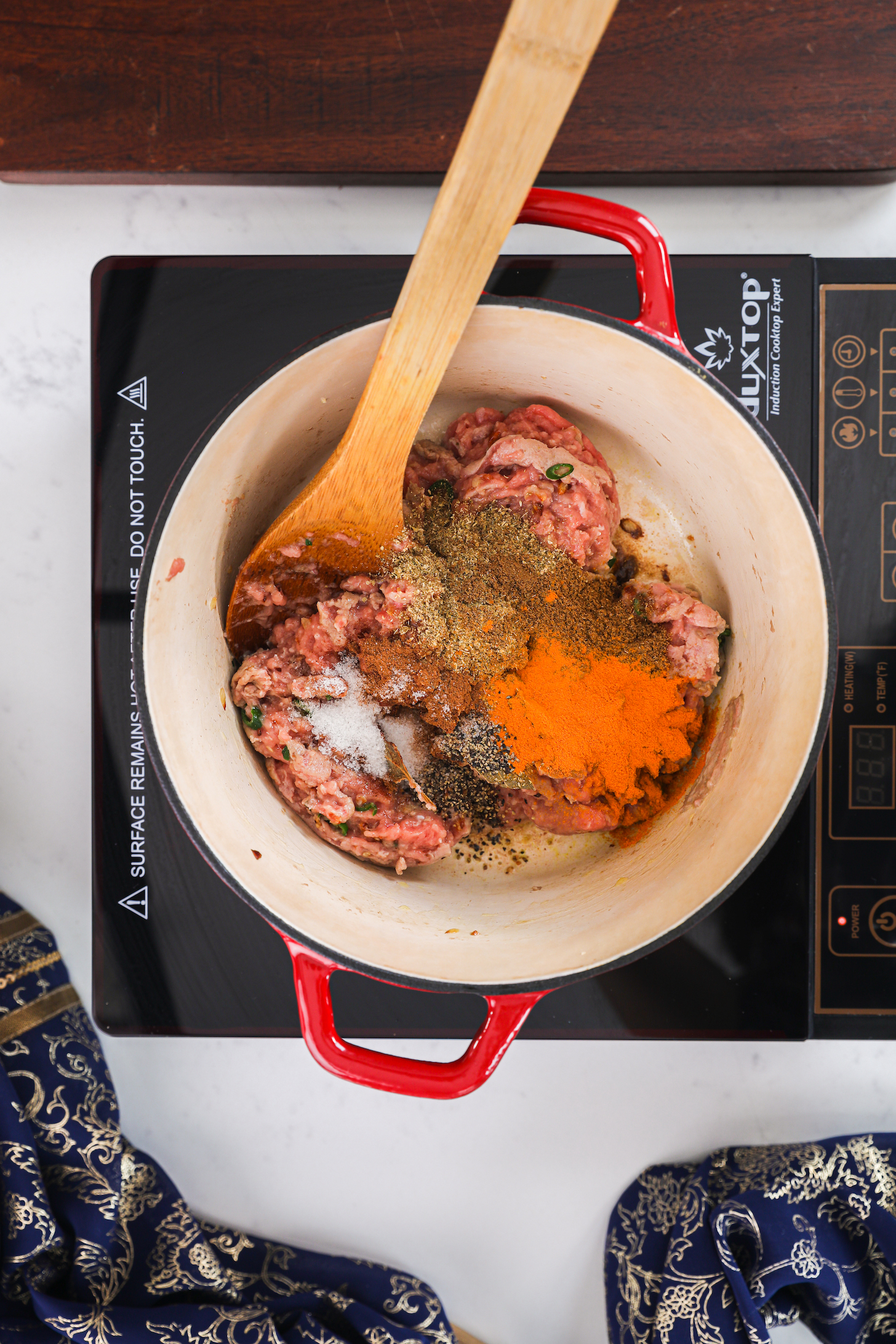 A pot of raw minced chicken topped with colourful spices on a mobile cooktop.