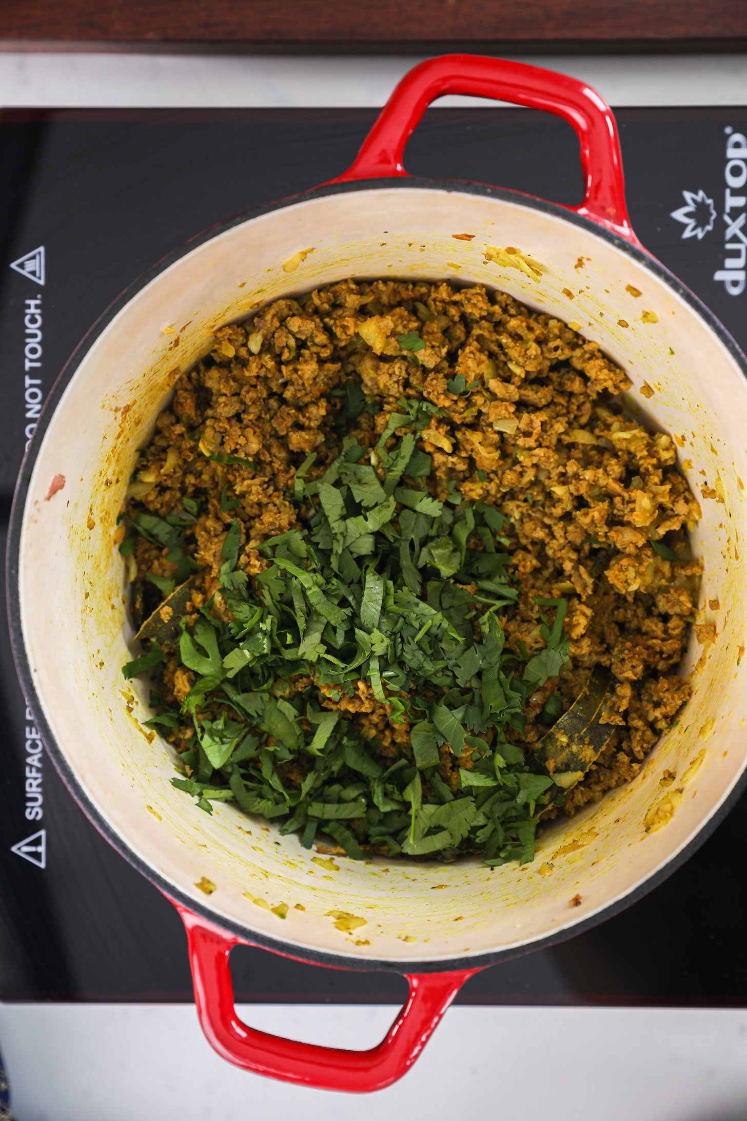 A pot of minced chicken topped with cilantro on a mobile cooktop.