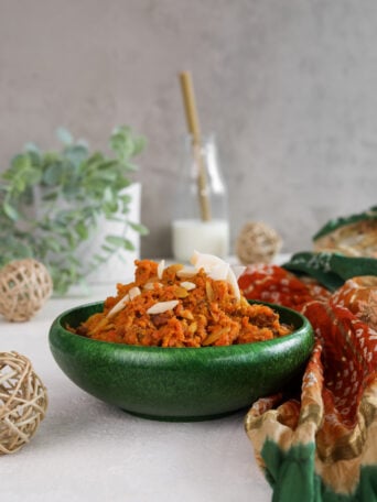 A green bowl of shredded carrots topped with nuts with a bottle of milk in the background.