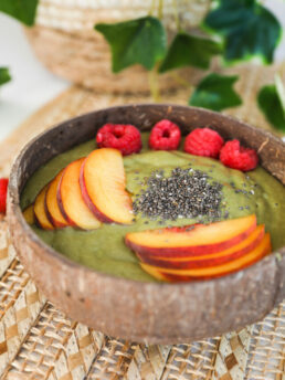 Perspective shot of a green smoothie bowl topped with chopped peached, berries and seeds.